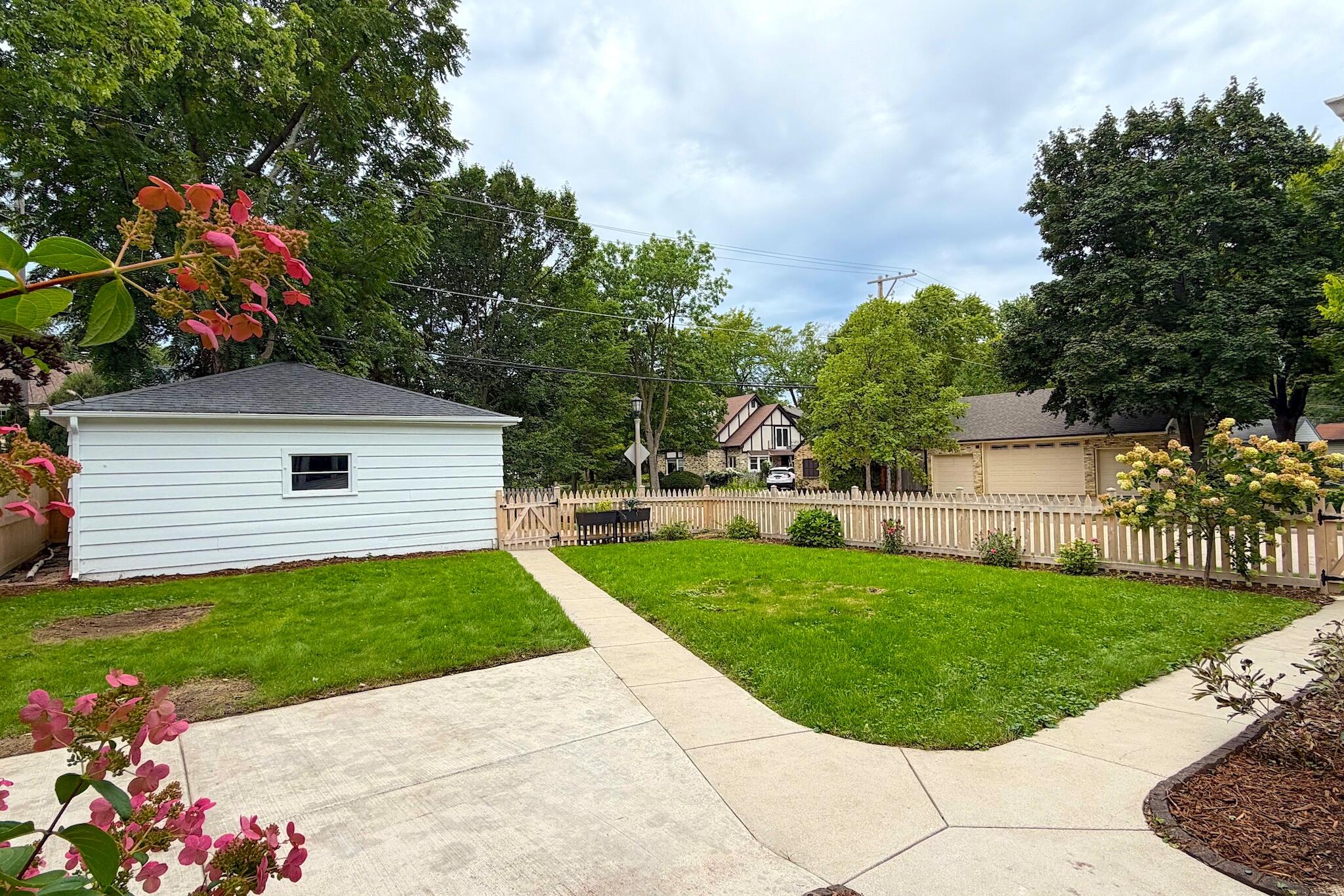 Backyard with a broad lawn, concrete walkways, white detached garage, and picket fence.