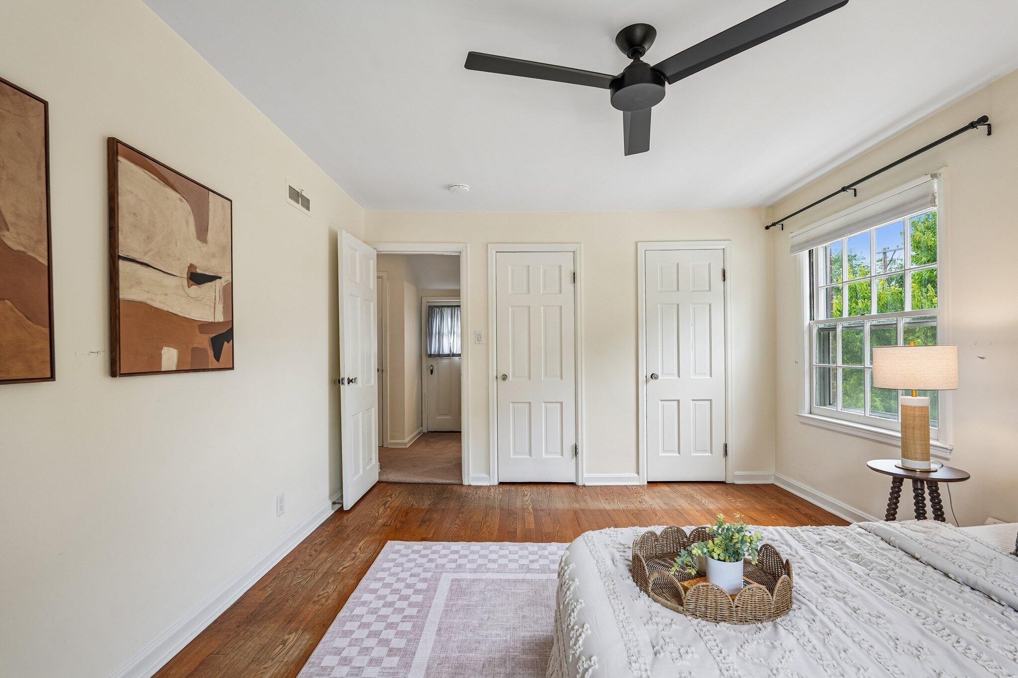 Staged bedroom with a large window, hardwood floors, and a black ceiling fan.