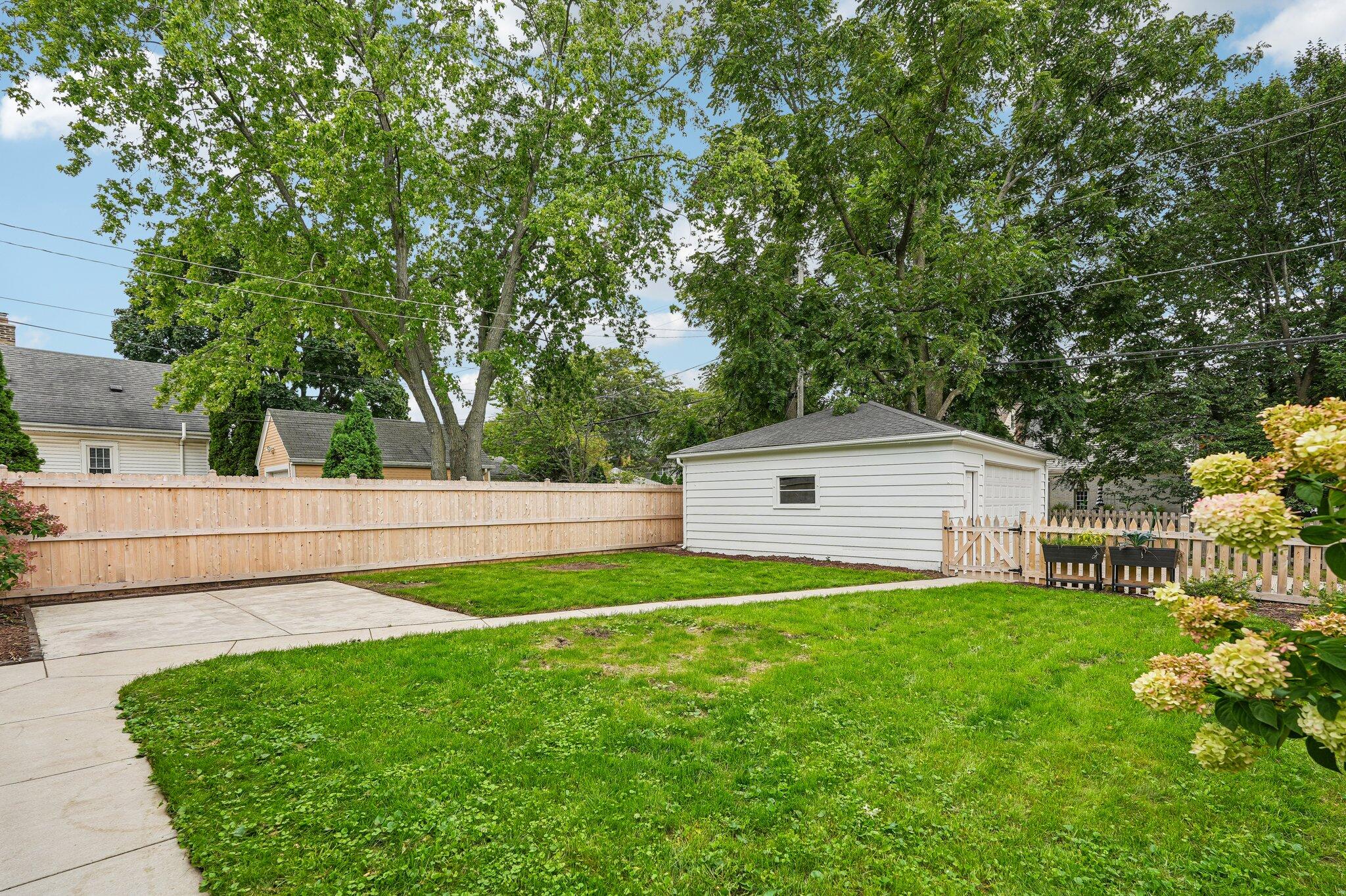 Backyard with a green lawn, concrete patio, detached garage, and wooden fencing.