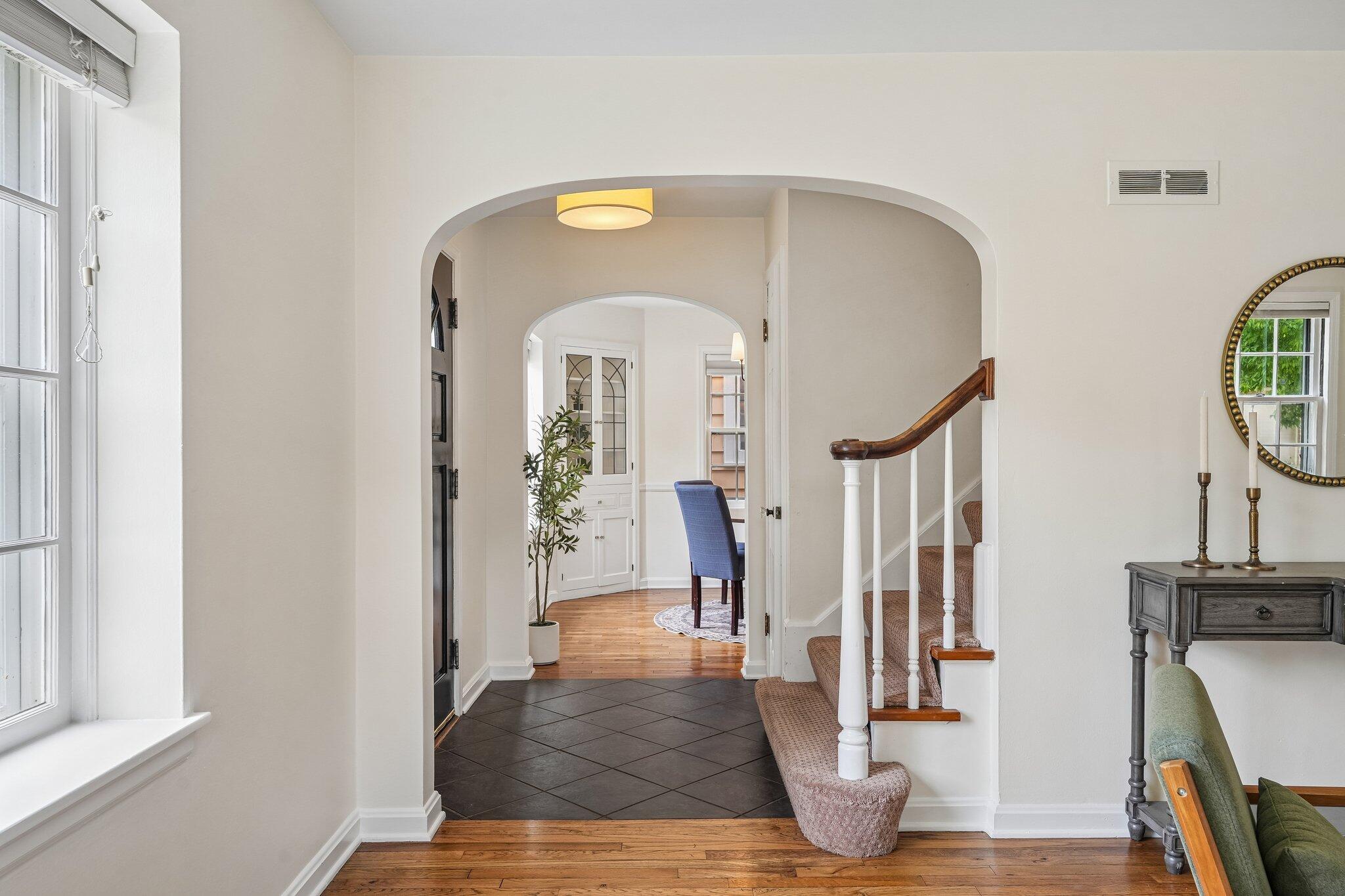 Entry hall with arched doorway, dark tile floor, and carpeted staircase with a wood handrail.