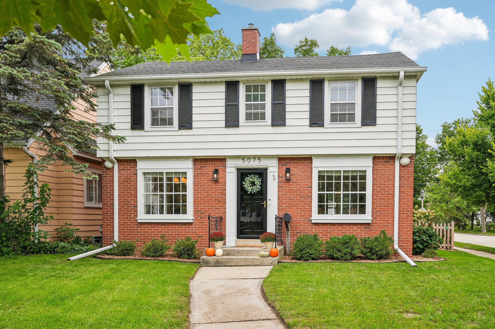 Two-story brick and white-sided home with black shutters, a curved front walk, and a green lawn.
