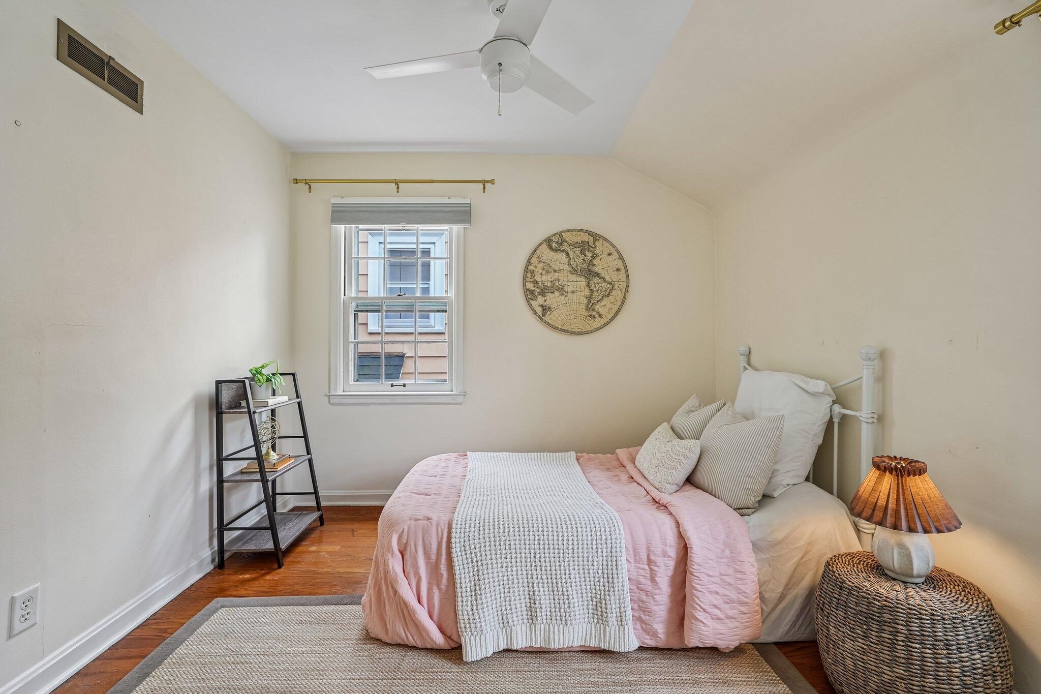 Bedroom with pink-and-white bedding, hardwood floors, and a round map on the wall.
