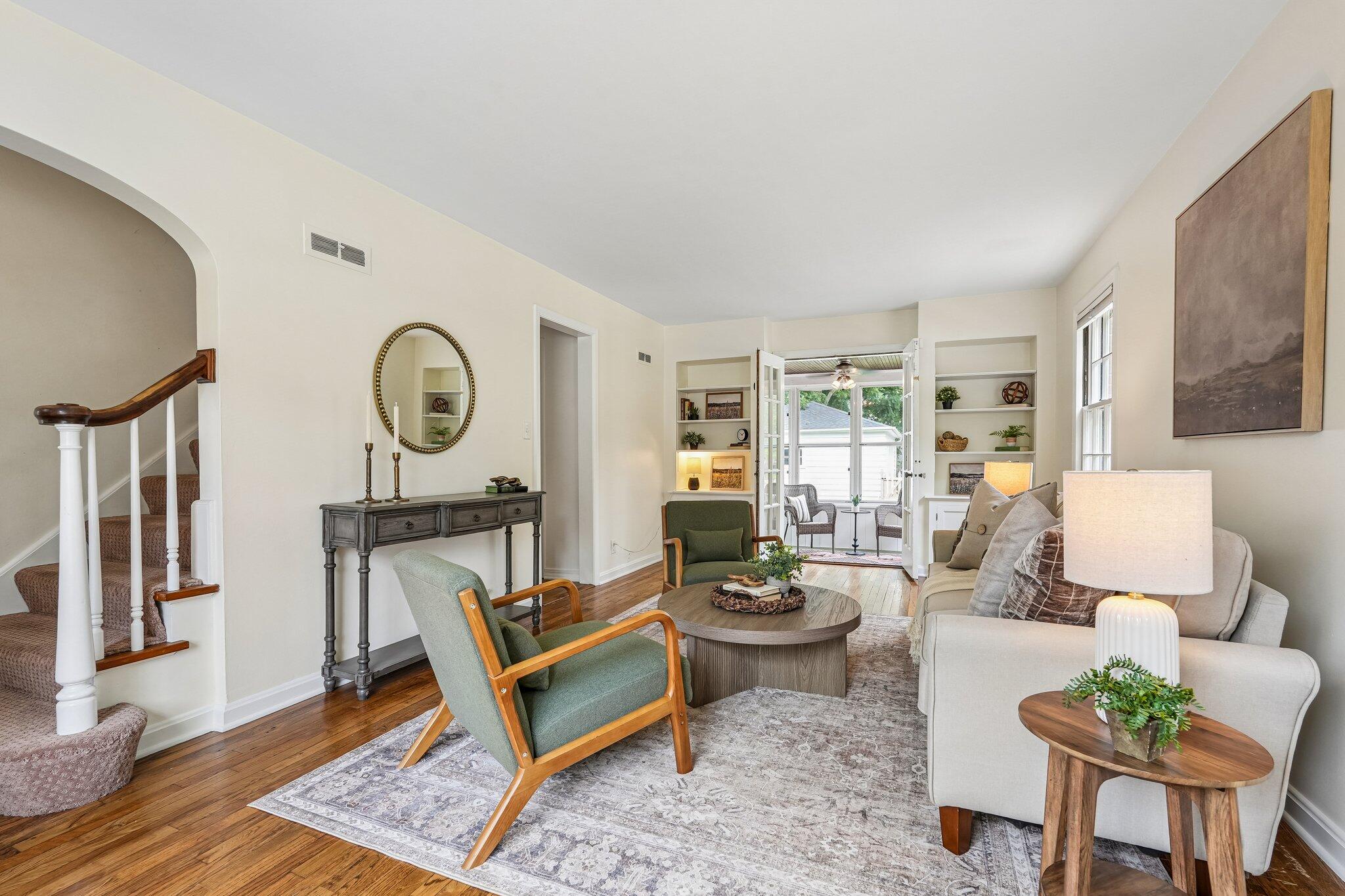 Furnished living room with hardwood floors, staircase, and open French doors to a sunroom.
