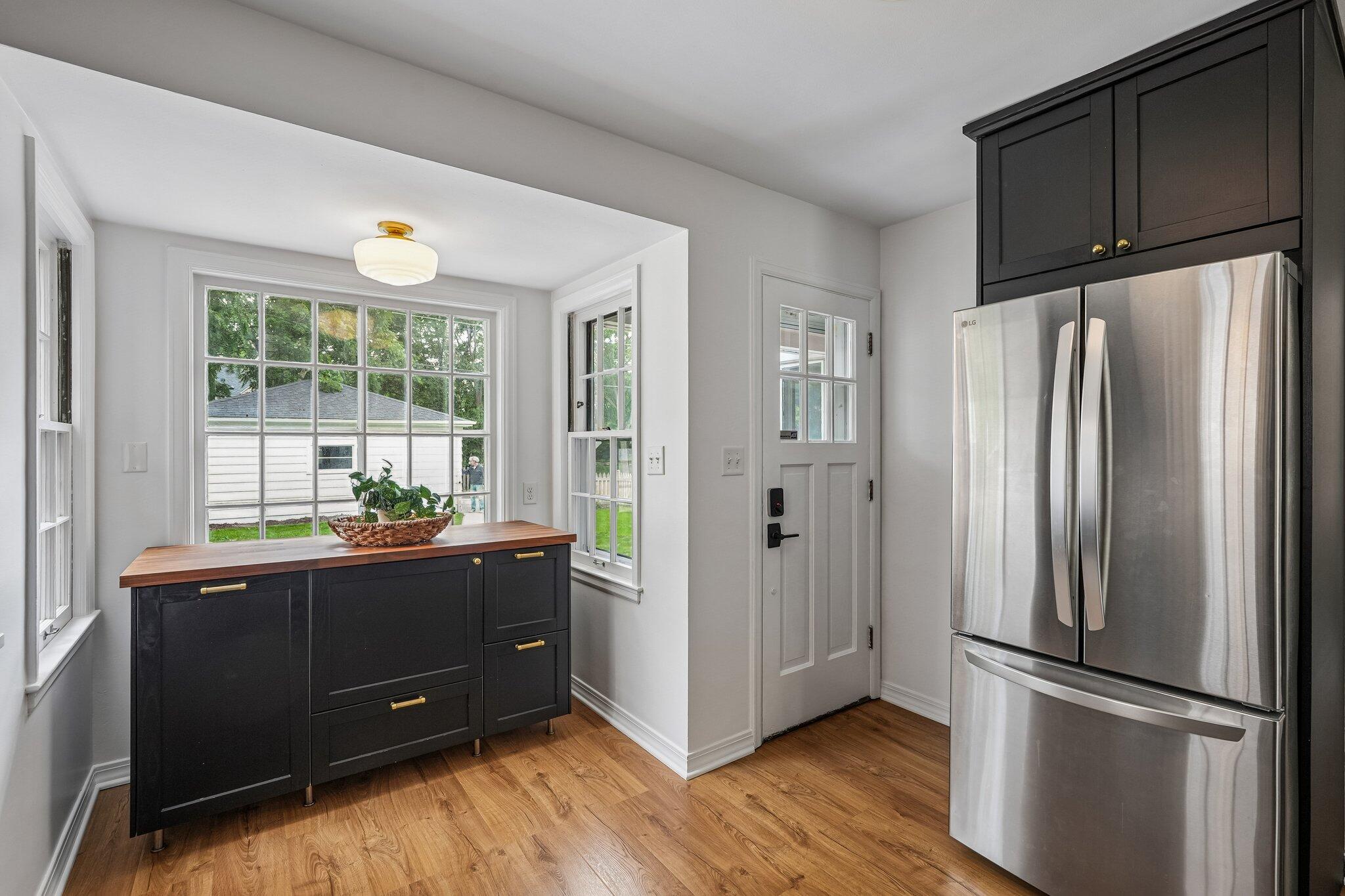 Kitchen with black cabinetry, butcher-block island, stainless steel refrigerator, and wood floors.