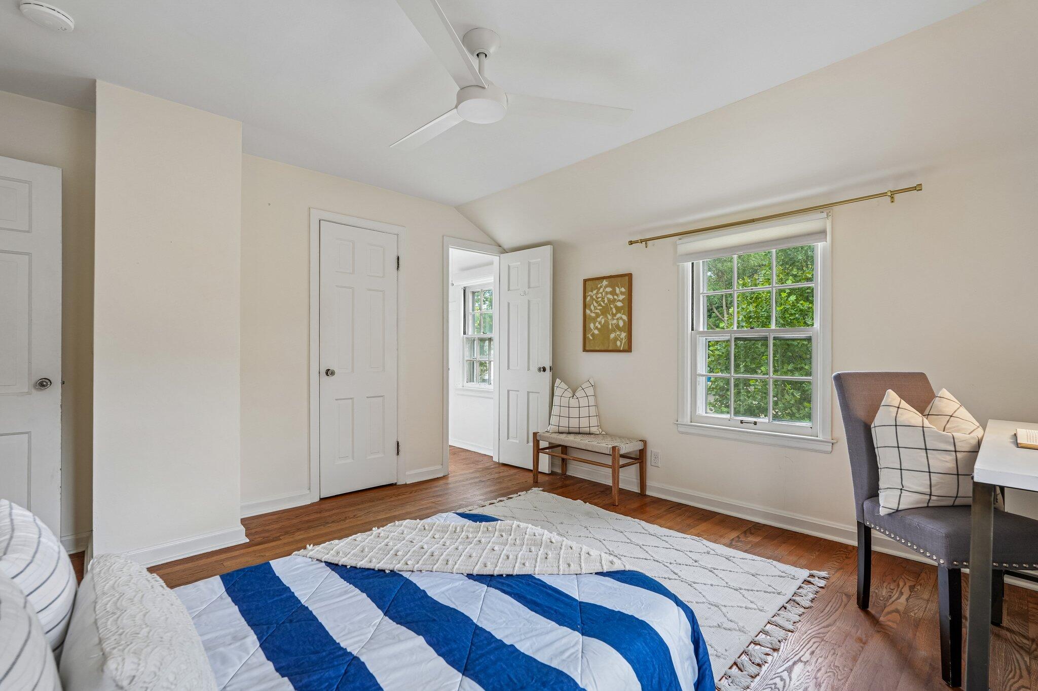 Bedroom with a blue-and-white striped bedspread, hardwood floors, and a window overlooking leafy trees.