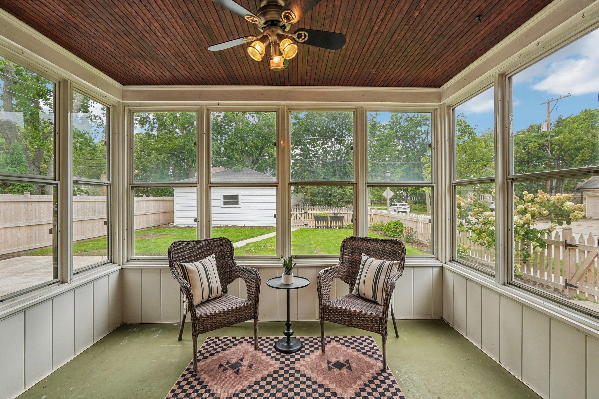 Enclosed porch with wicker chairs and large windows overlooking a fenced yard.