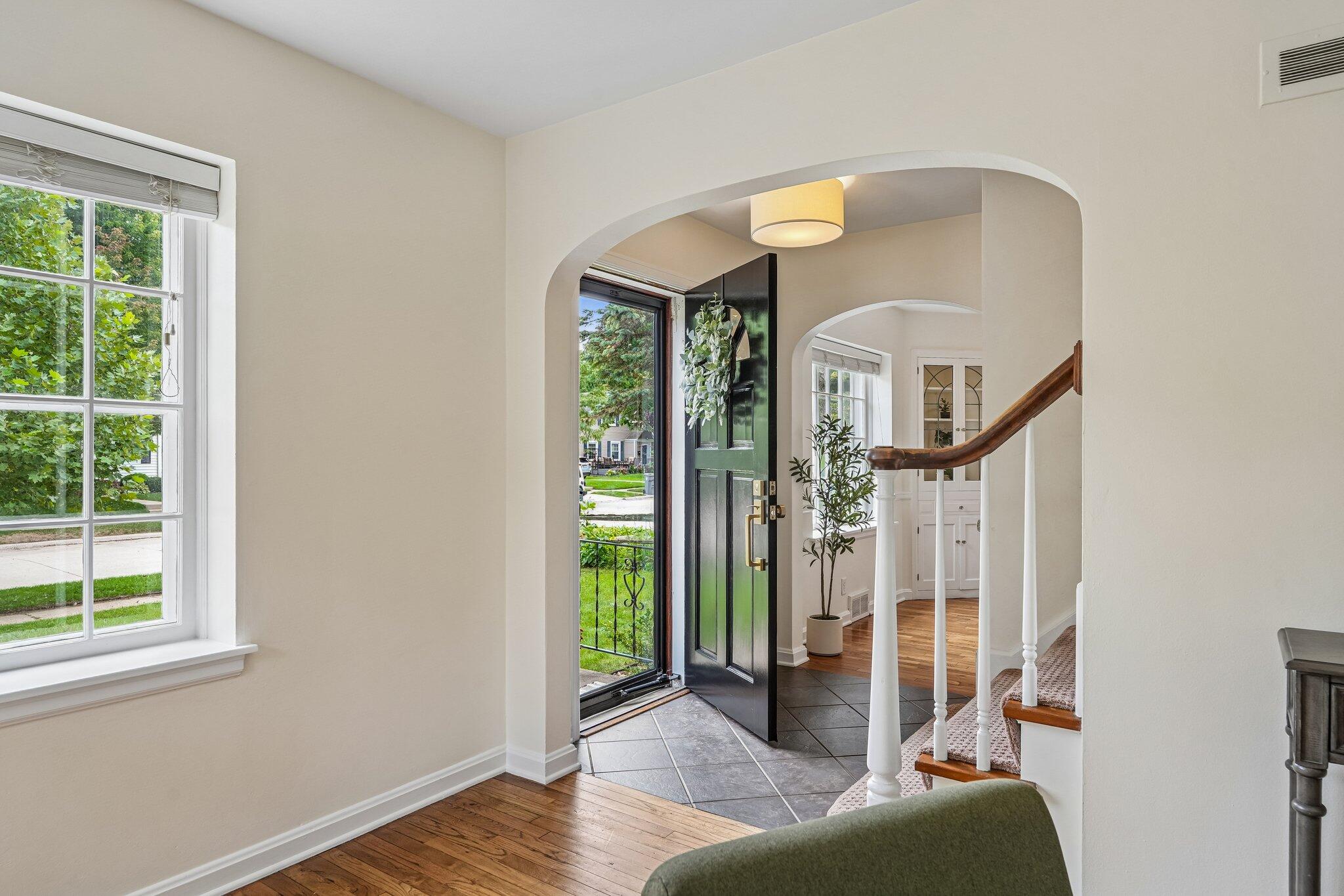 Entry hall with an open dark front door, arched passages, and a carpeted staircase.