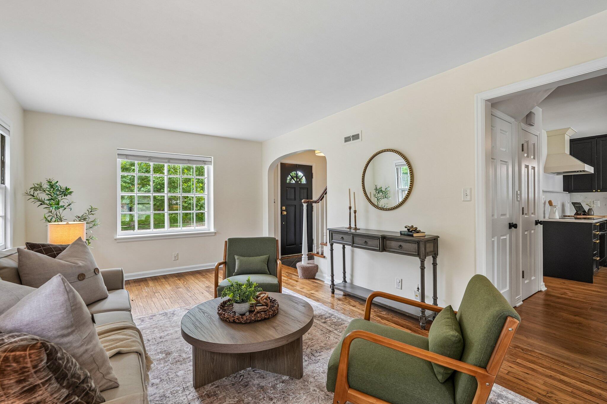 Living room with green armchairs, a gray sofa, wood floors, and an arched entry to the front door.