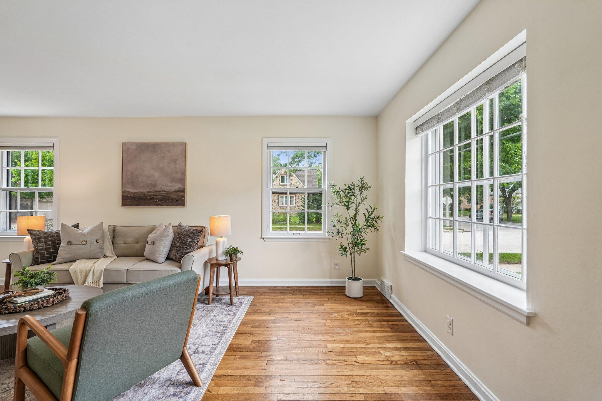 Living room with a beige sofa, green accent chair, hardwood floors, and large windows.