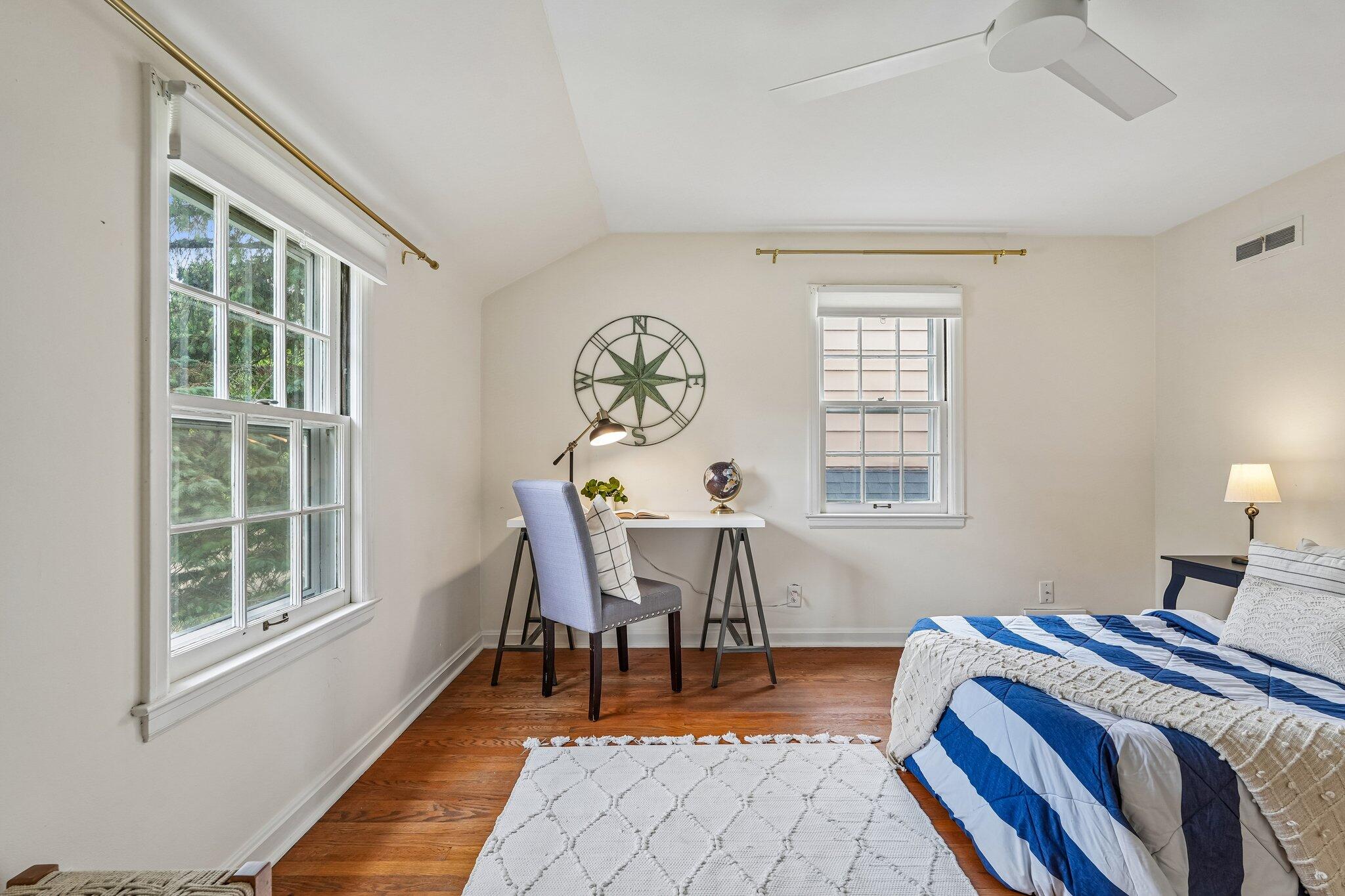 Bedroom with a blue-and-white quilt, hardwood floors, and a desk beneath a compass wall decoration.