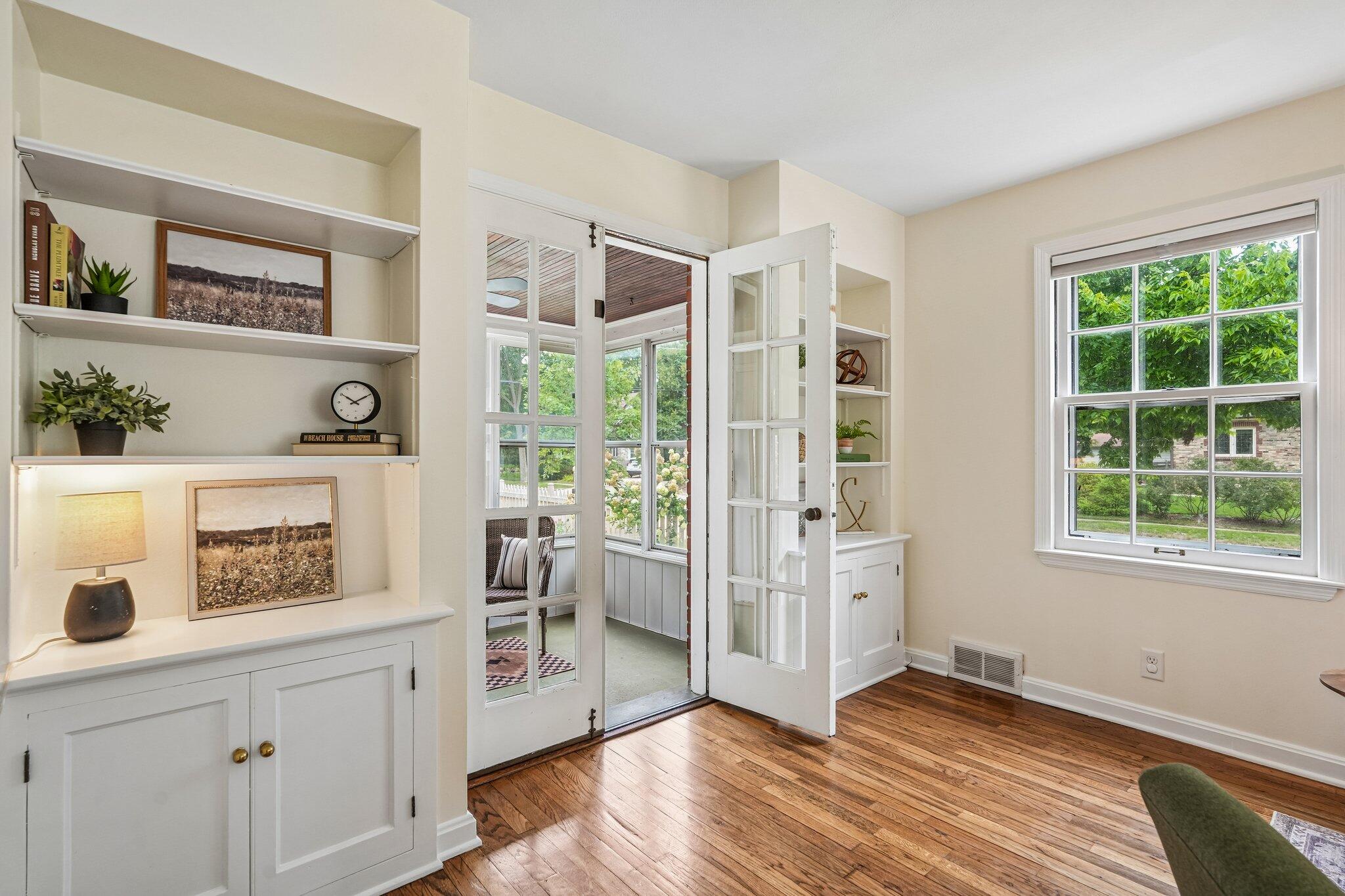 Bright room with built-in shelving, hardwood floors, and French doors opening to an enclosed porch.