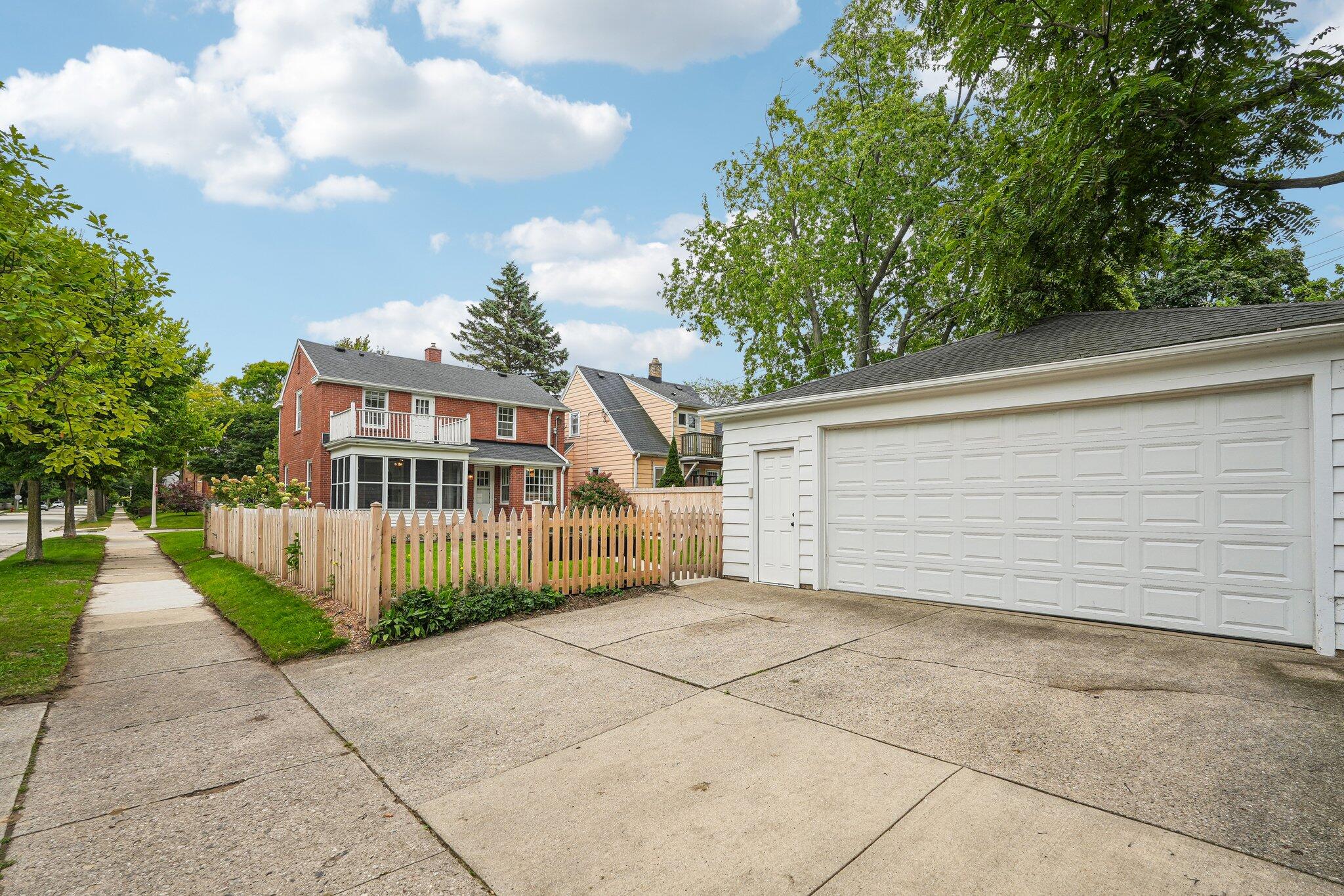 Red-brick house behind a picket fence, beside a large white garage and driveway.