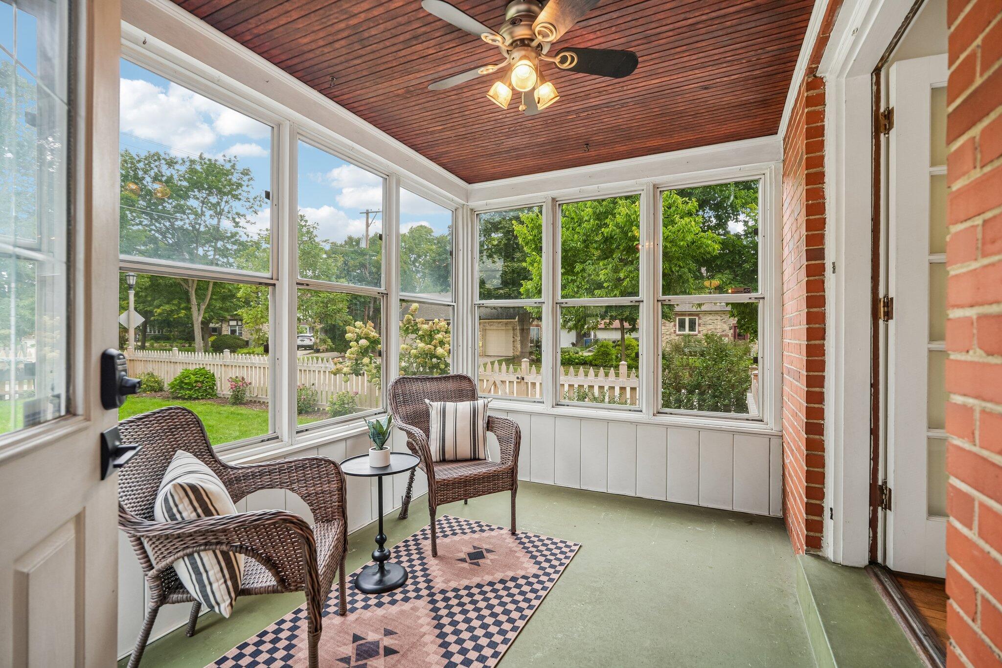 Sunroom with wicker seating, a wood-paneled ceiling, and large windows overlooking a fenced yard.