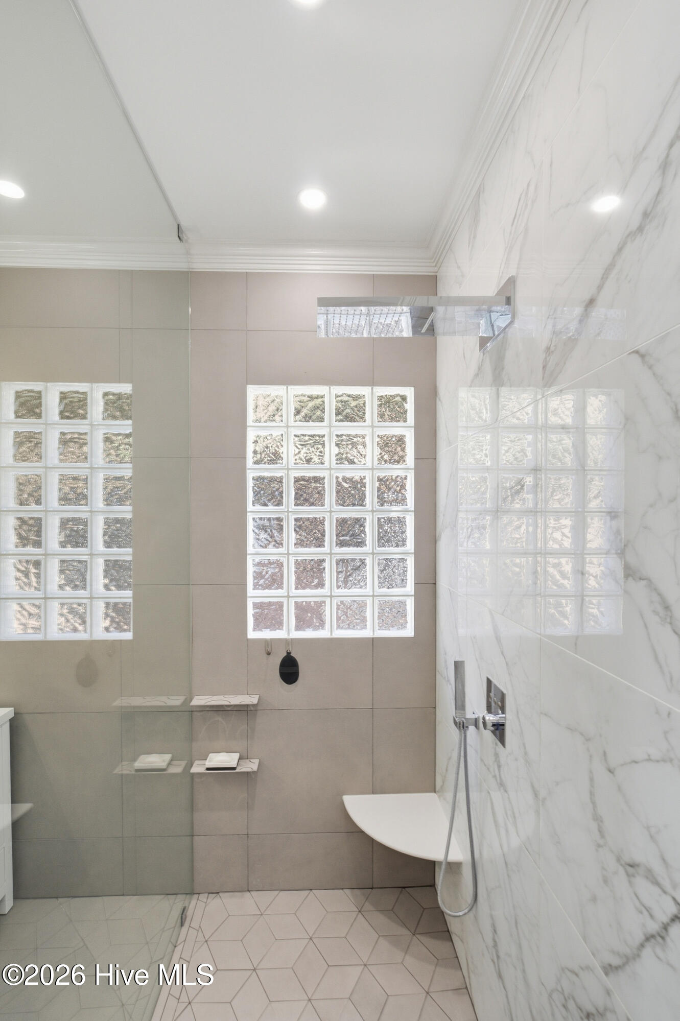 Modern bathroom shower with marble-patterned walls, glass-block windows, and geometric floor tiles.