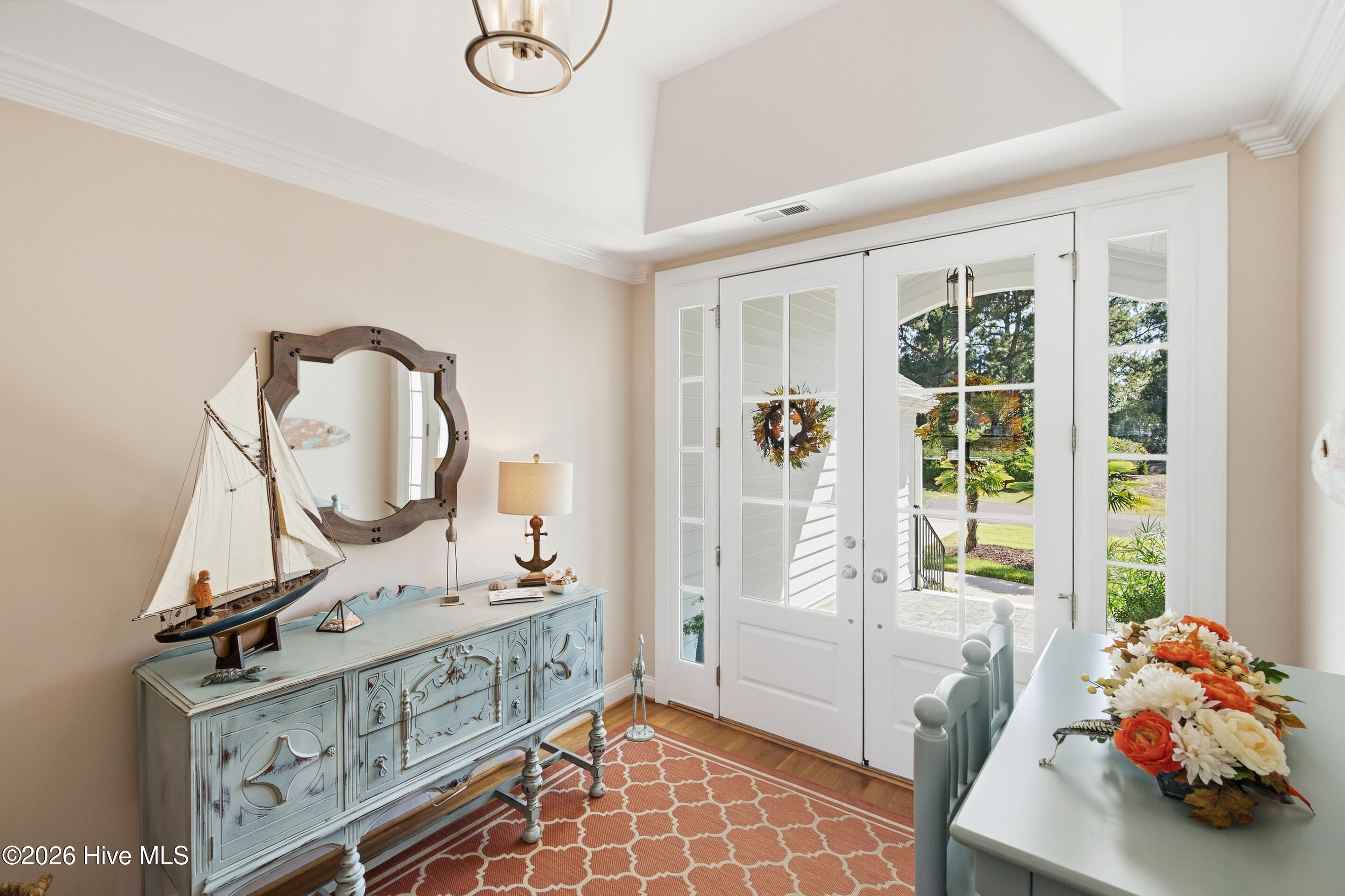 Dining room with a distressed blue console, model sailboat, floral centerpiece, and glass-paneled doors to the garden.