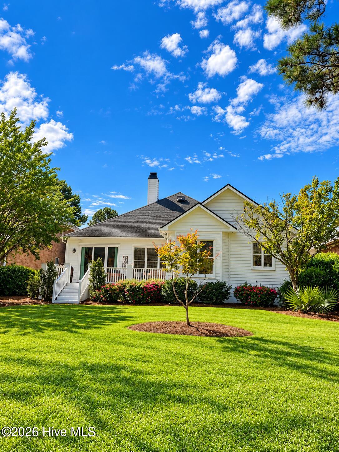White-sided house with a gabled roof, front porch, landscaped flower beds, and a broad green lawn.