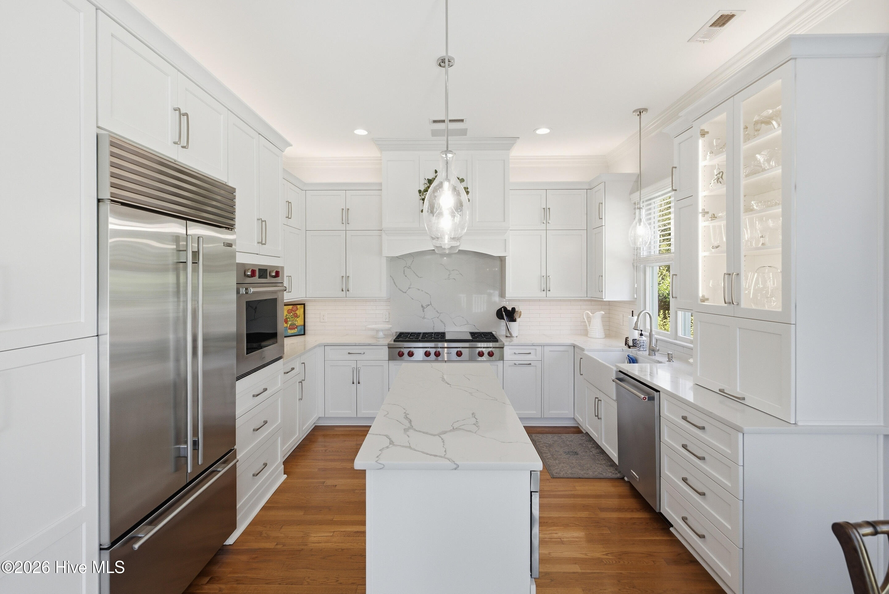 Bright white kitchen with a marble-look island, stainless steel appliances, and glass-front cabinets.