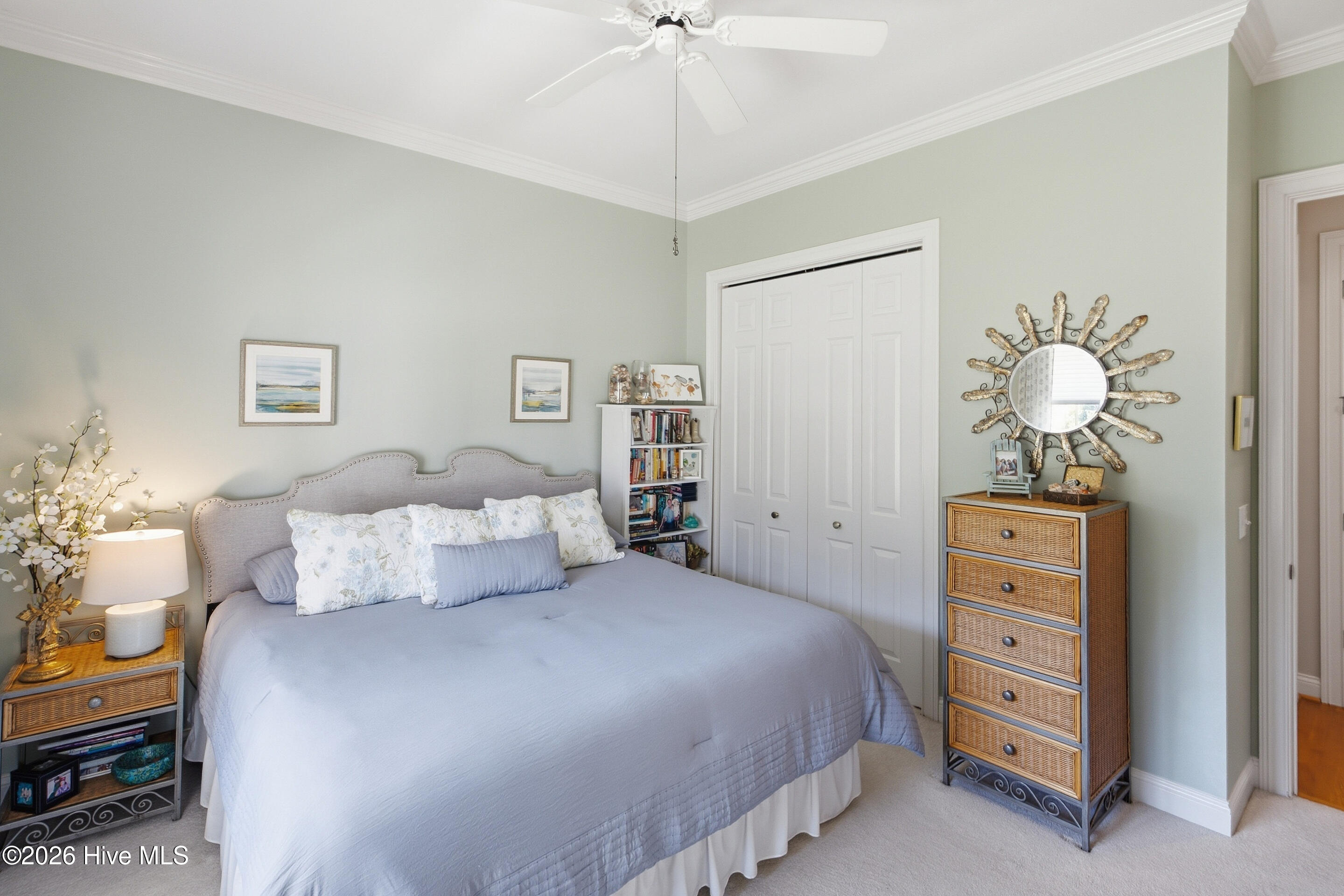 Bedroom with a light blue-gray bedspread, pale sage walls, and woven-front dressers.