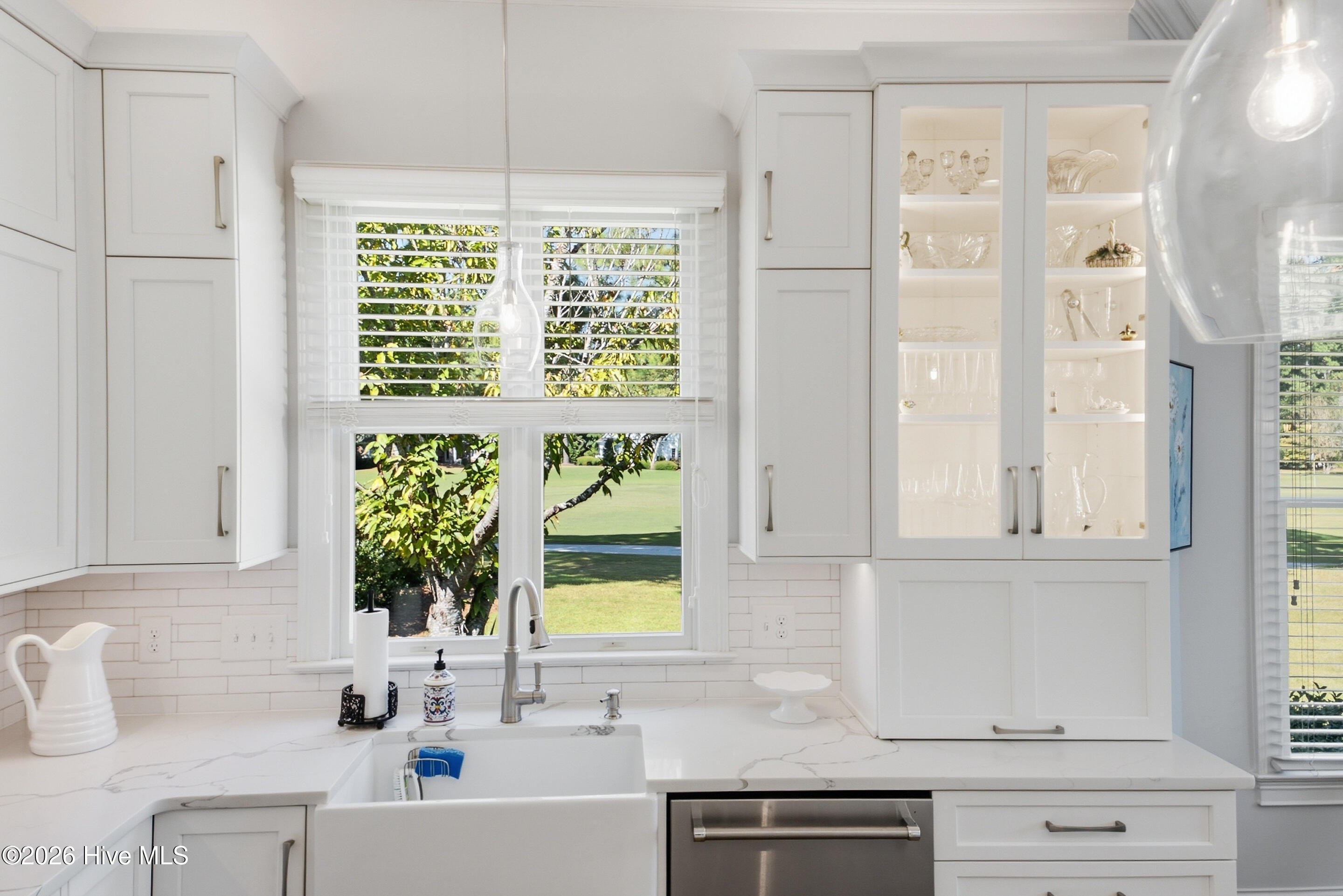 White kitchen with a farmhouse sink and glass-front cabinets overlooking a lawn.