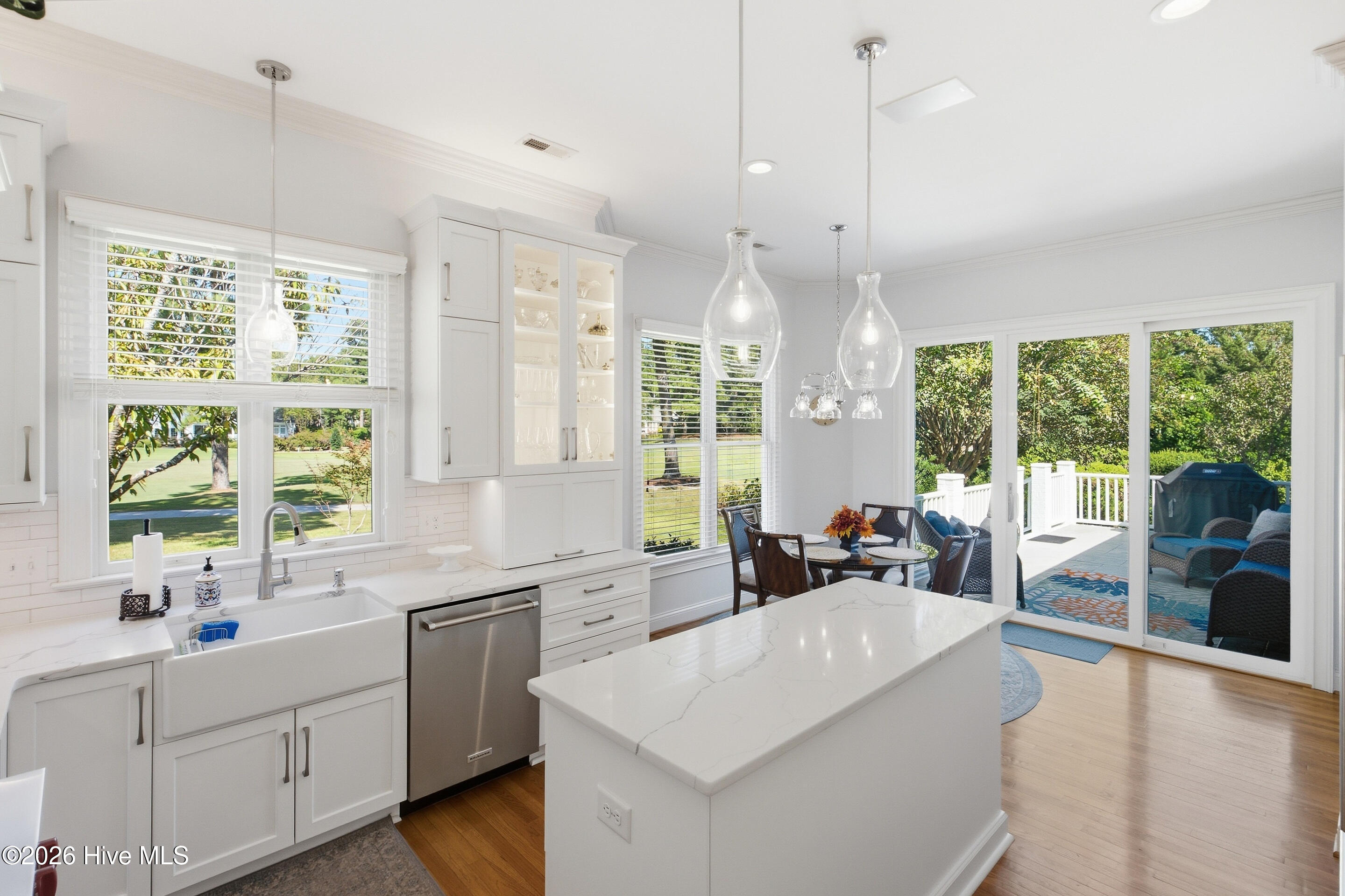 Bright white kitchen with a large island, glass-front cabinets, and sliding doors opening to a furnished deck.