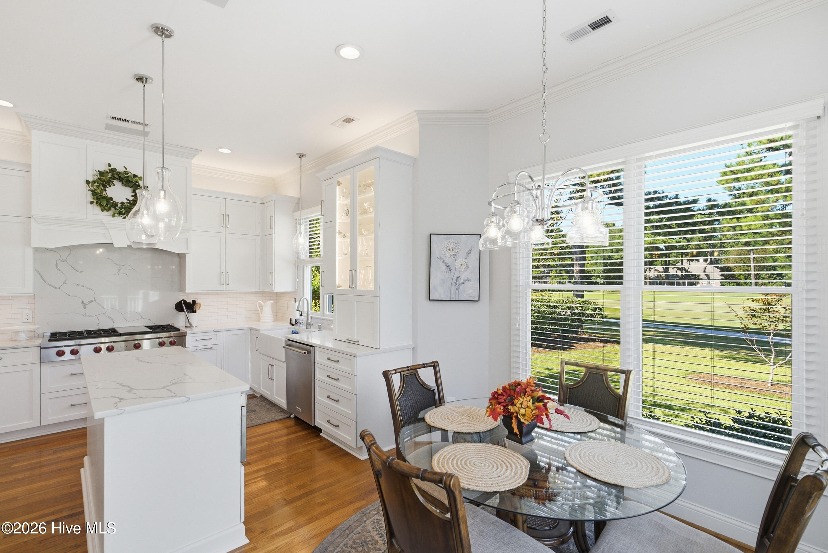Bright white kitchen with marble-look island and glass dining table beside windows overlooking a lawn.