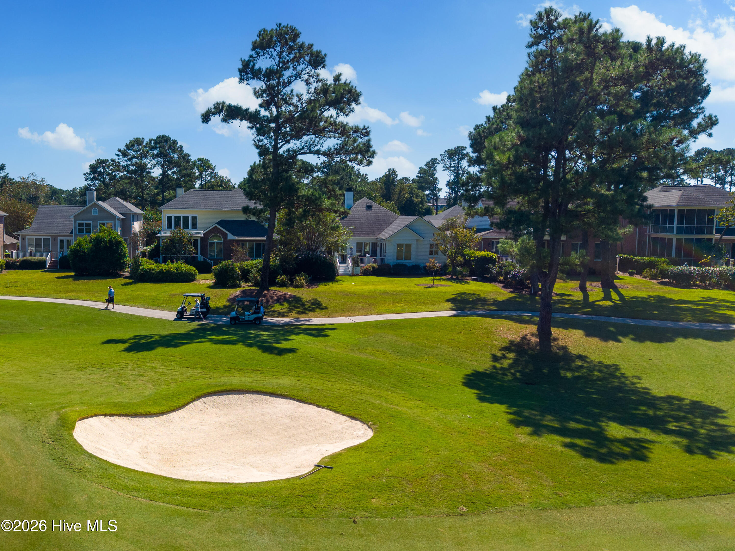 Aerial view of homes bordering a golf green, with a sand bunker and golf carts.