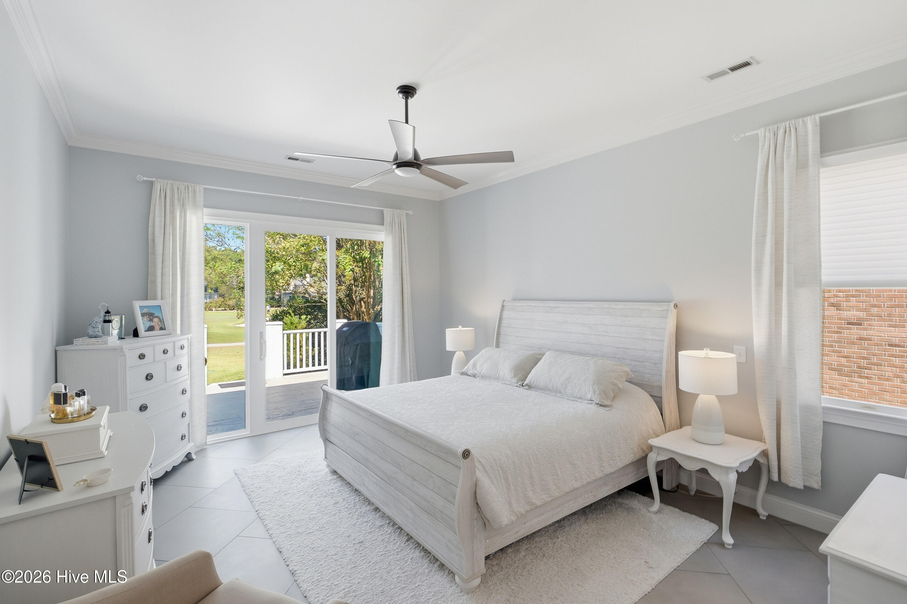 Bedroom with a white bed and sliding glass doors opening to a patio and green lawn.
