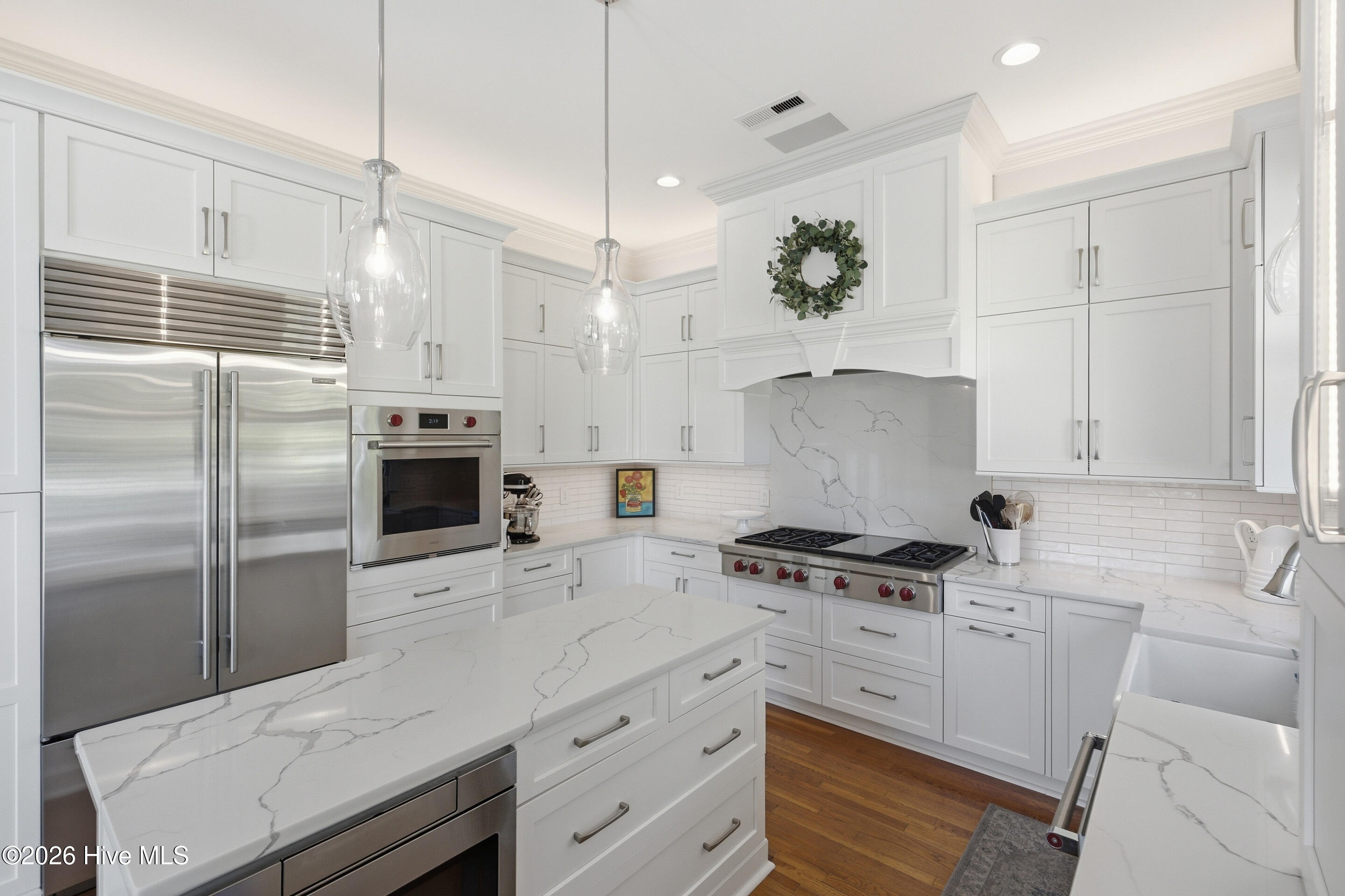 White kitchen with a veined stone island, stainless steel appliances, and a wide gas range.