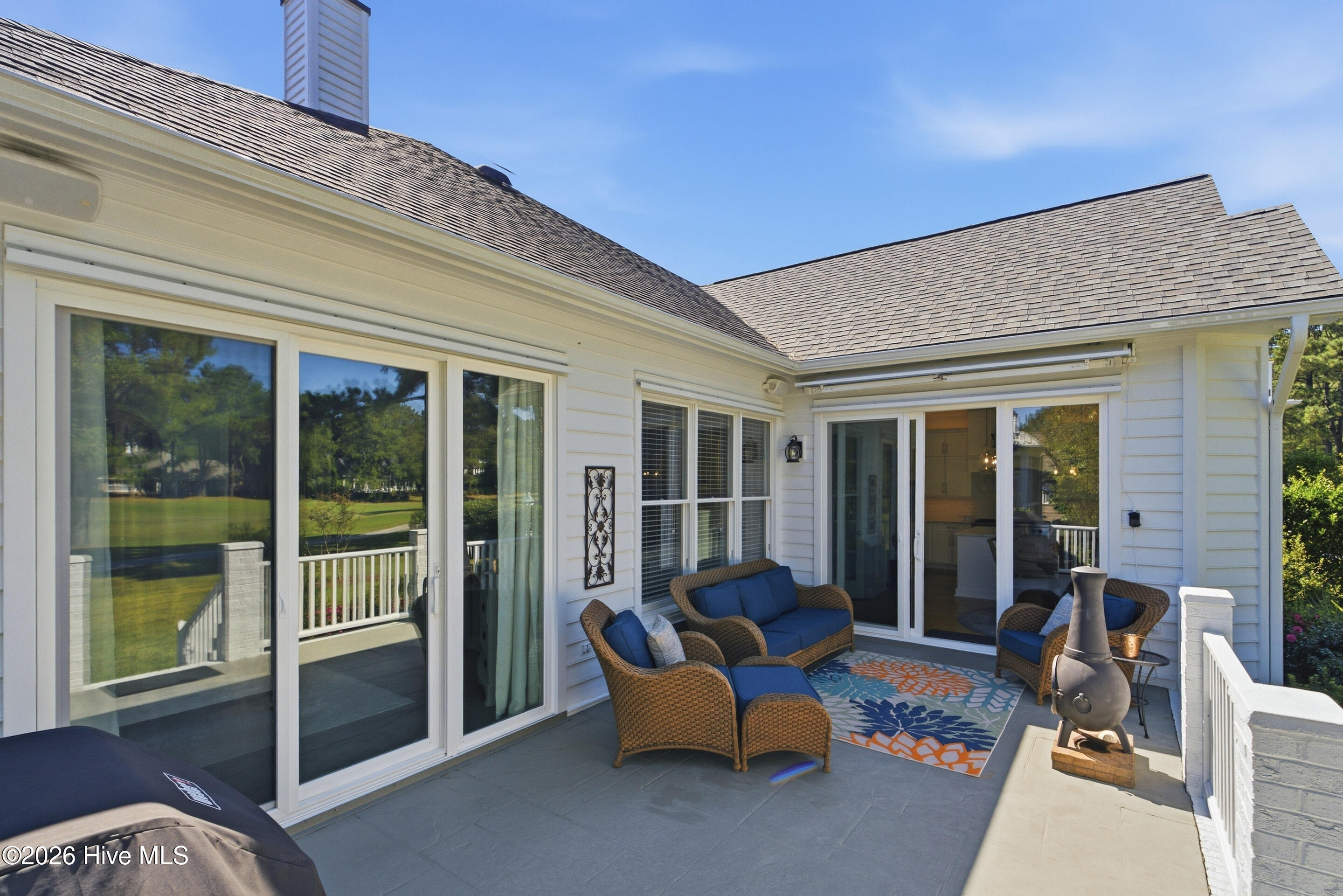 Outdoor patio with wicker seating, blue cushions, a colorful rug, and a freestanding chiminea.