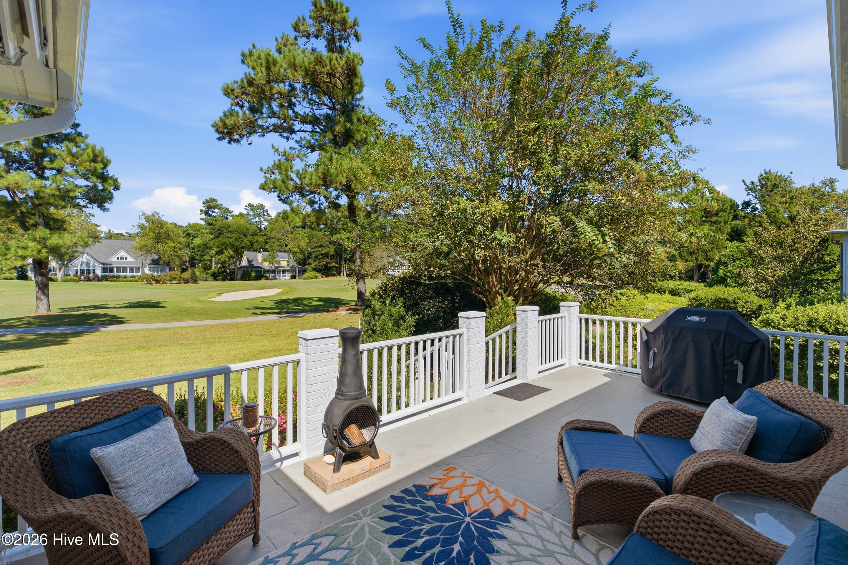 Furnished patio overlooking a golf course, with wicker seating, a chiminea, and a covered grill.