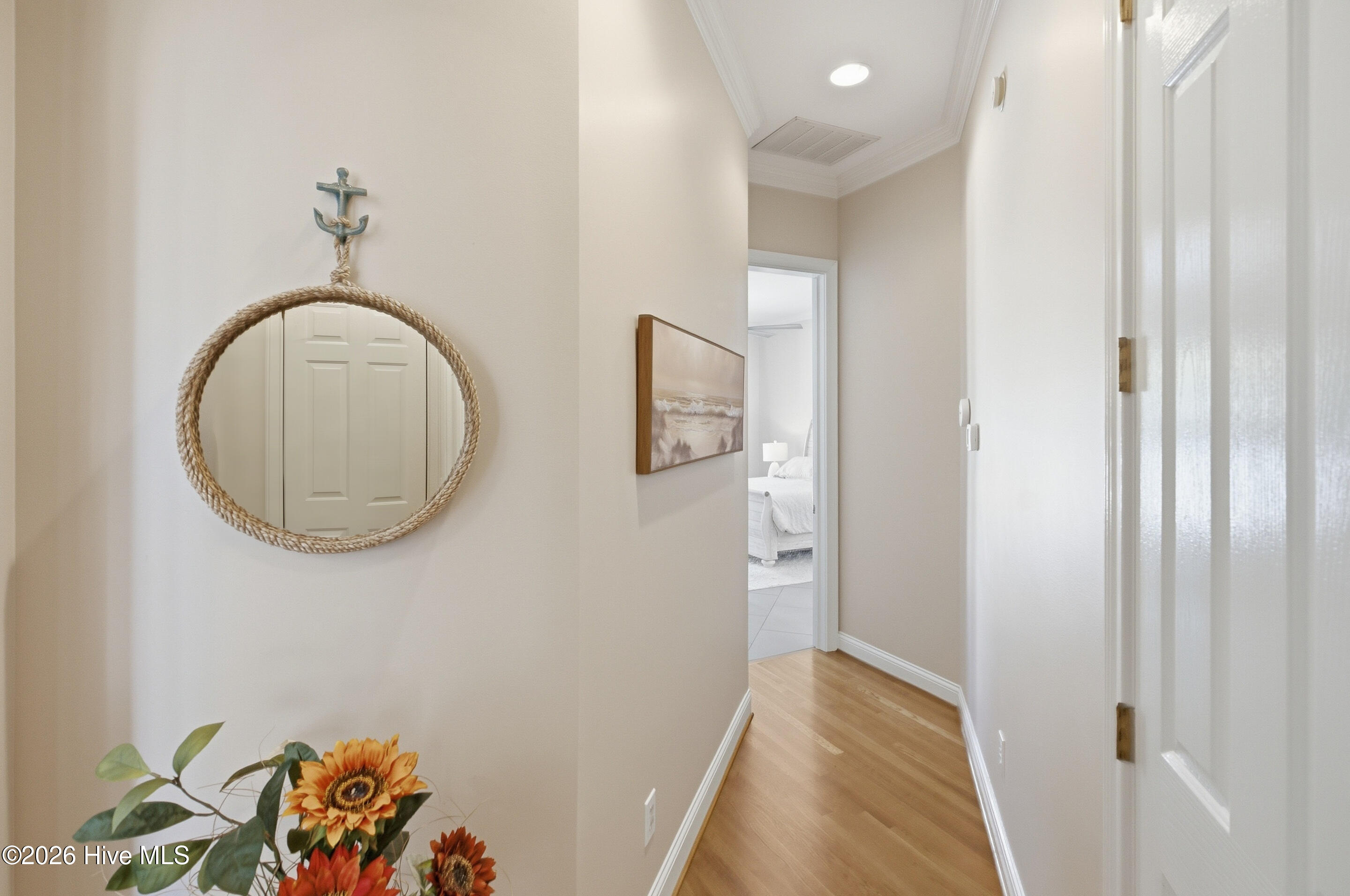 Hallway with a rope-framed mirror, sunflower arrangement, and bedroom visible through an open doorway.