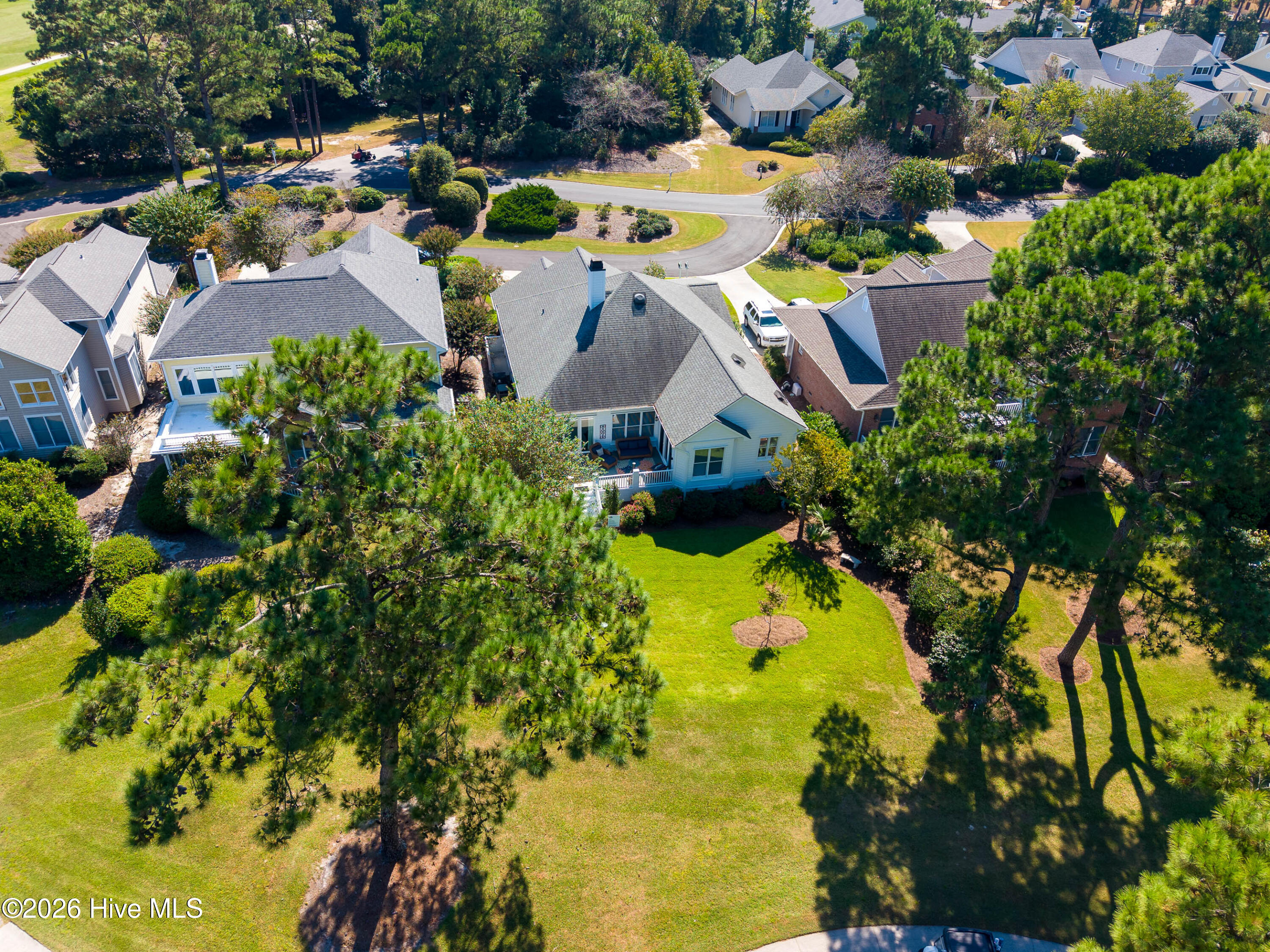 Aerial view of a house with a rear patio, broad lawn, and mature trees.