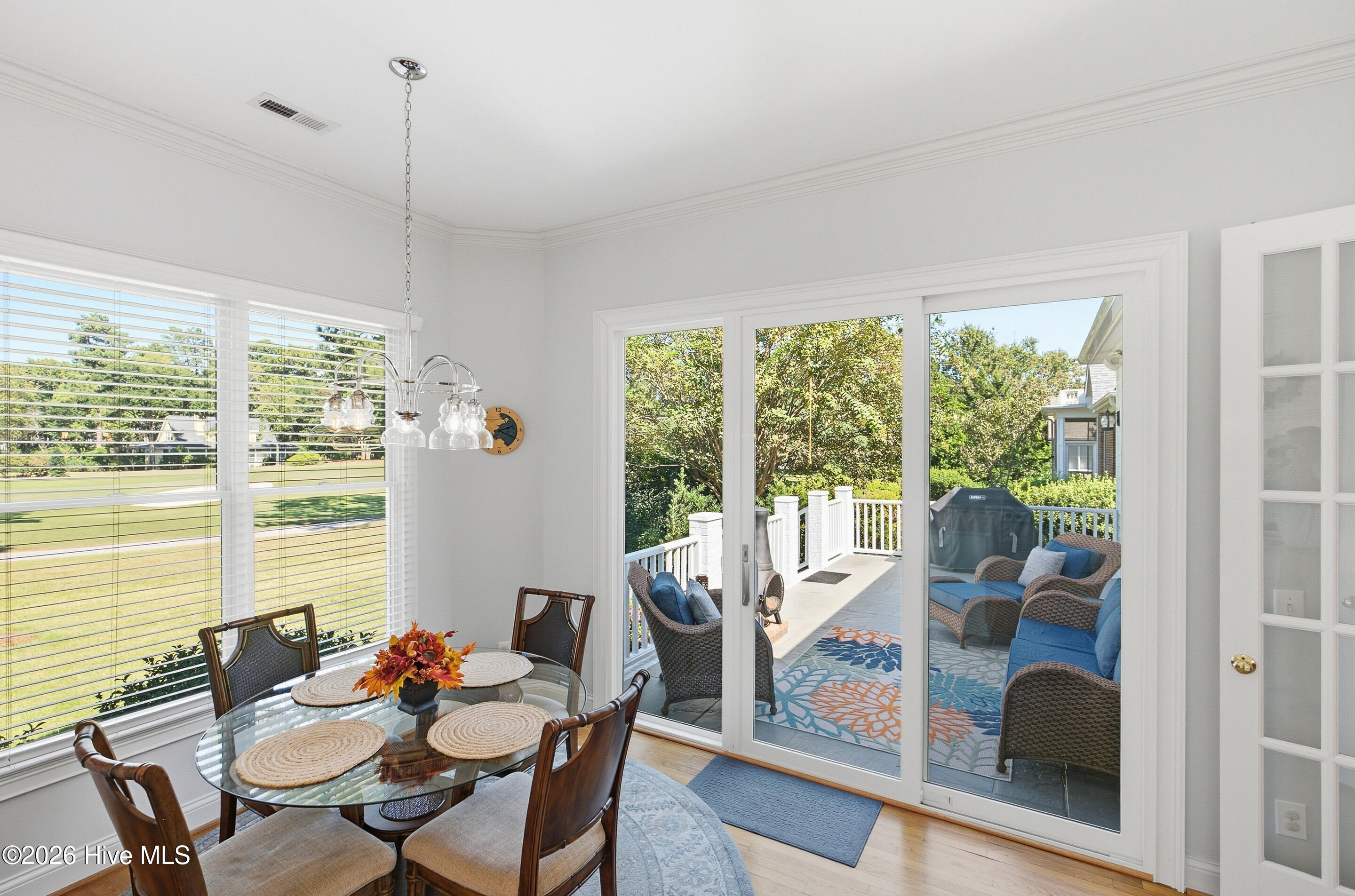 Dining area with glass-top table and chairs, opening onto a furnished deck through sliding glass doors.