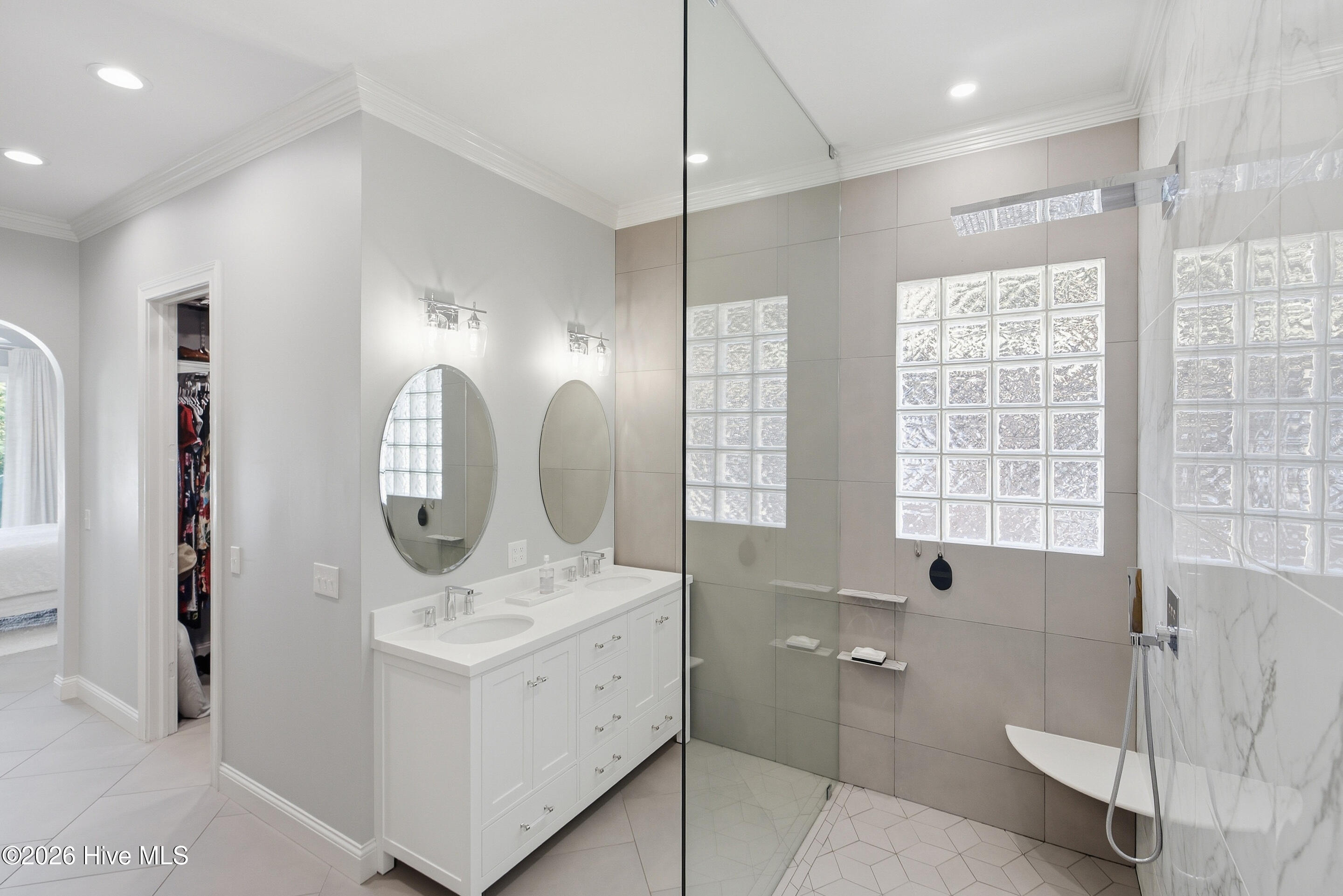 Bright bathroom with a double vanity, glass-enclosed shower, glass-block windows, and freestanding soaking tub.