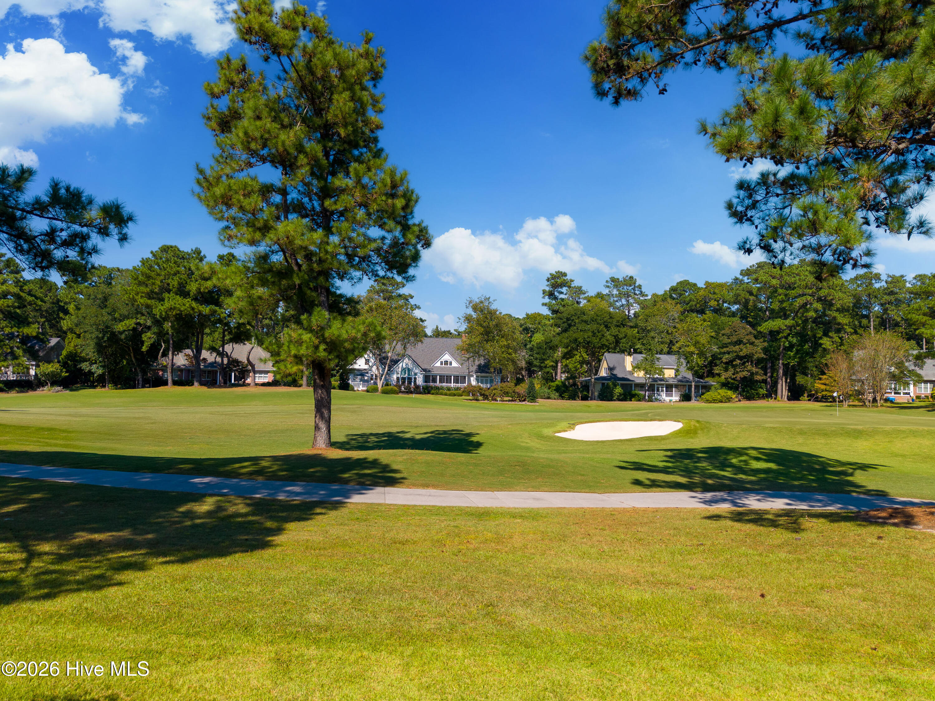 Golf course with a sand bunker, cart path, and homes beyond the green.