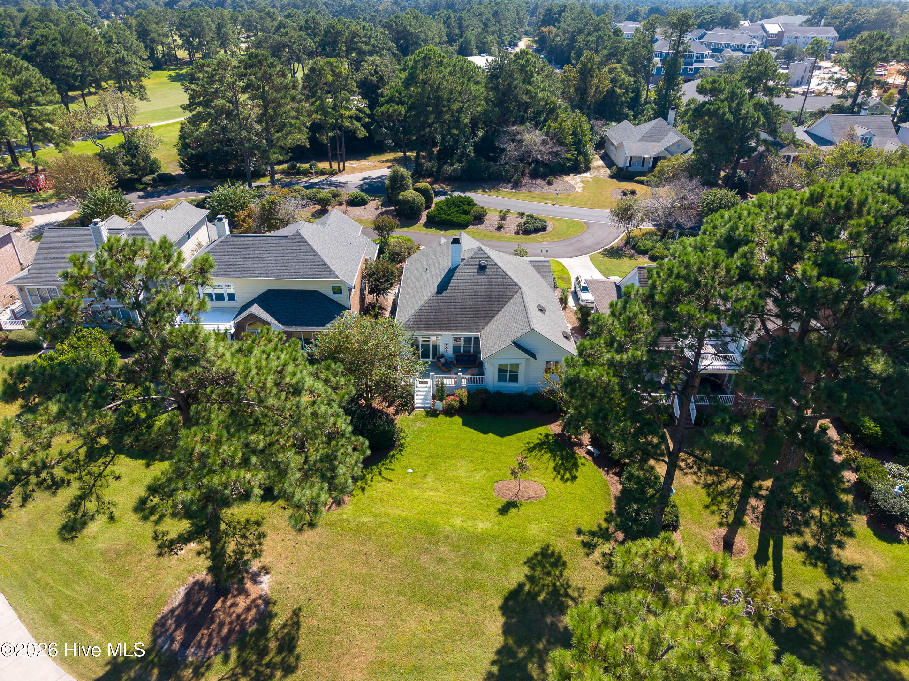 Aerial view of a home with a spacious lawn, mature pines, and a manicured golf-course area nearby.