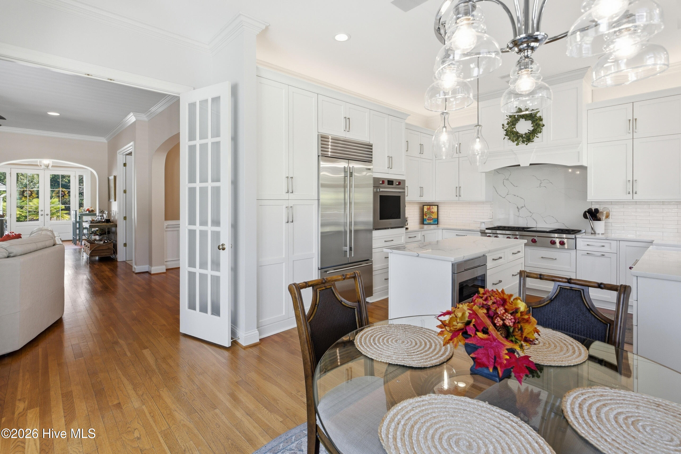 Bright white kitchen with a large island, stainless steel appliances, and glass pendant lights beside a dining table.
