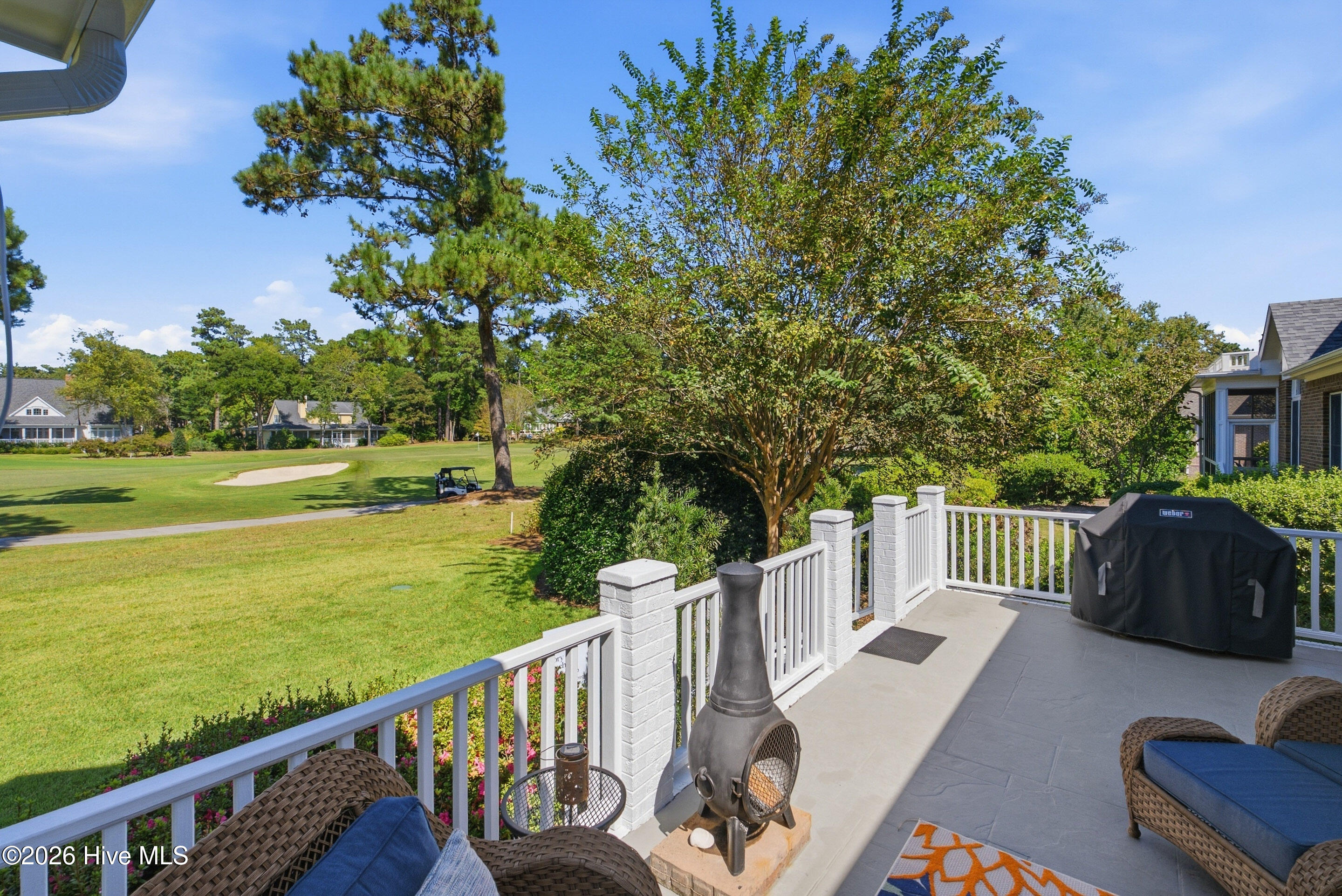 Patio overlooking a golf course, with white railings, wicker seating, and a chiminea.