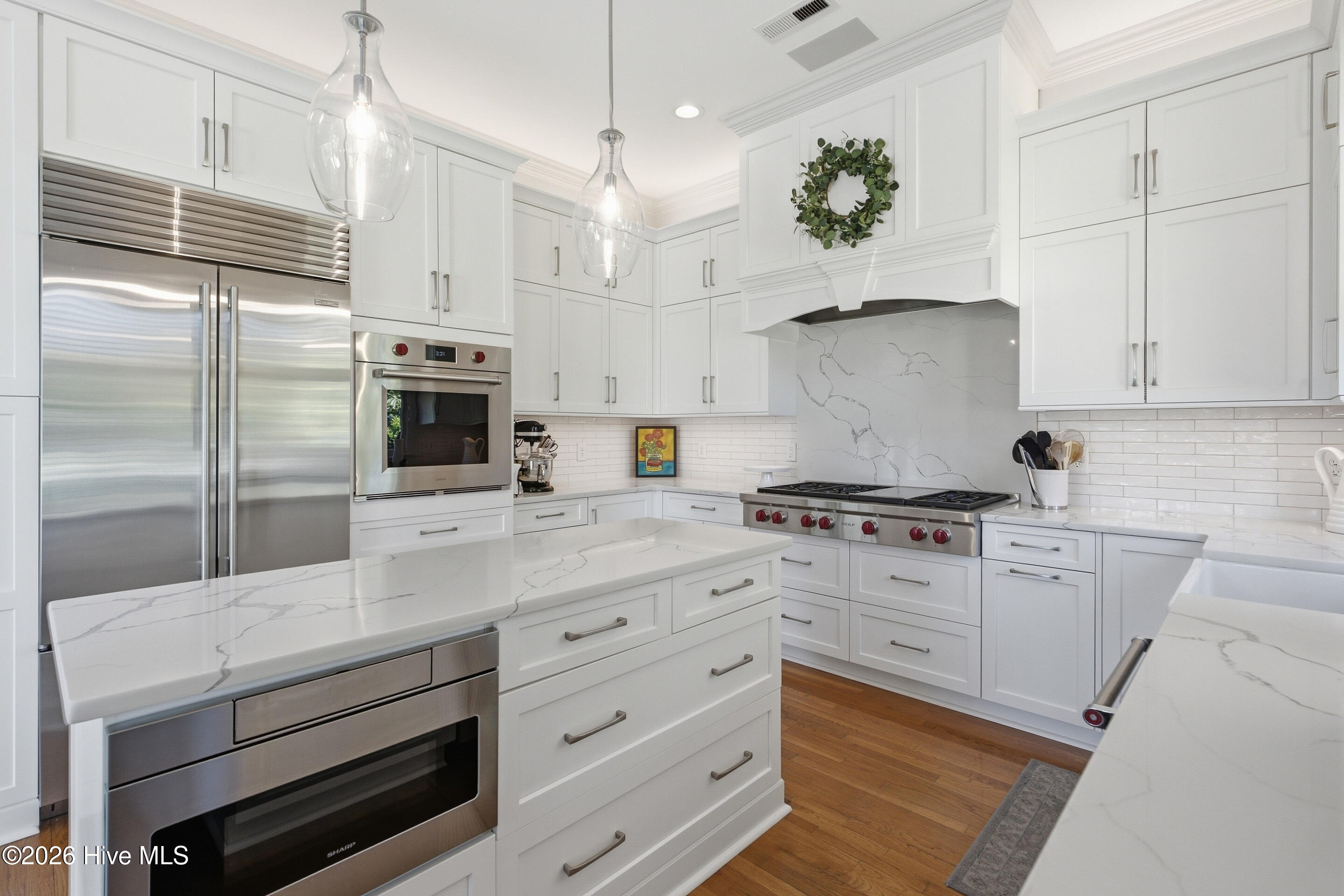 White kitchen with a large island, stainless steel appliances, and a veined stone backsplash.