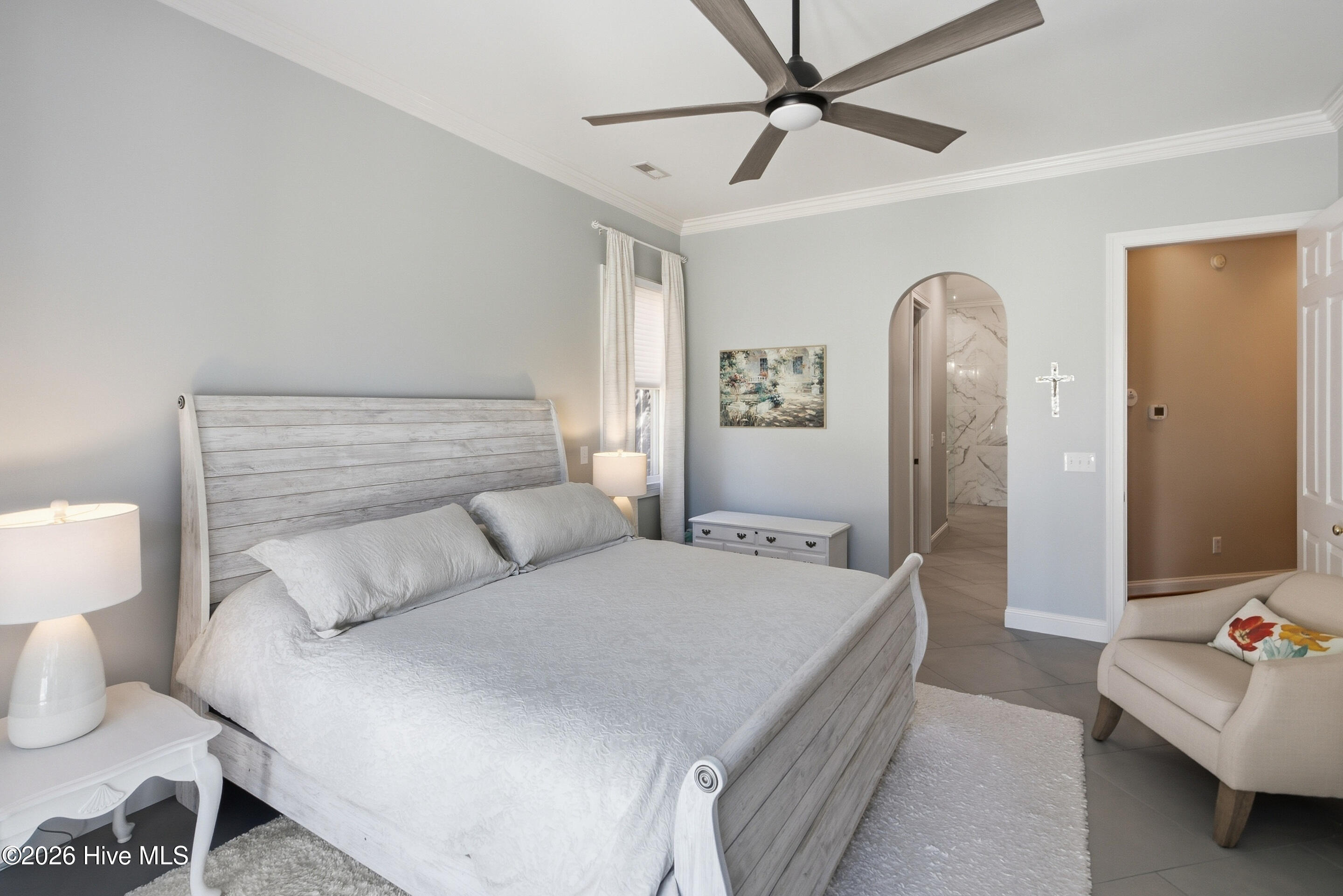Bedroom with a whitewashed wood bed, ceiling fan, and arched doorway to a marble-tiled bathroom.