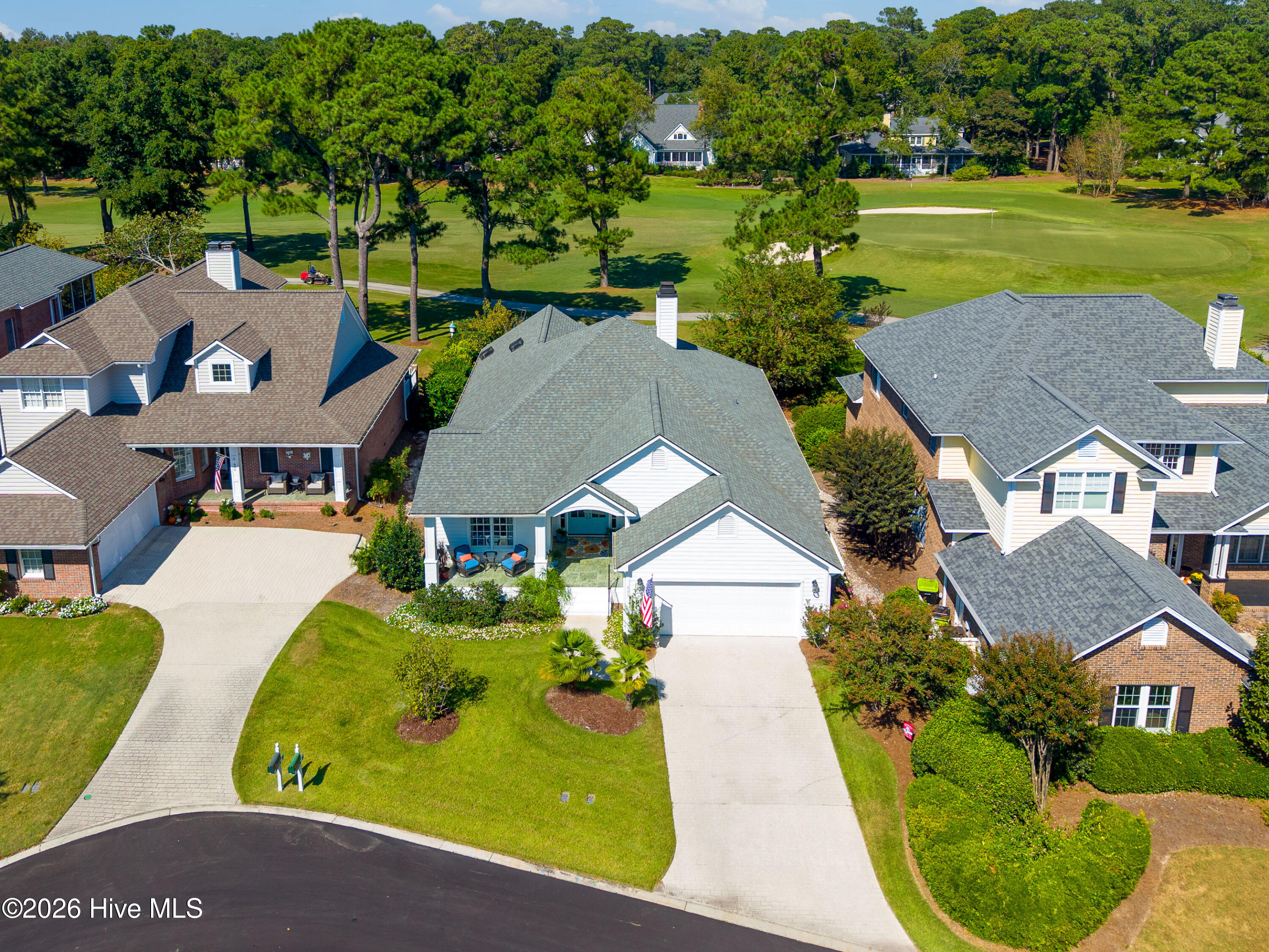 Aerial view of a gray-roofed home beside a golf course, with its driveway and landscaped front yard visible.