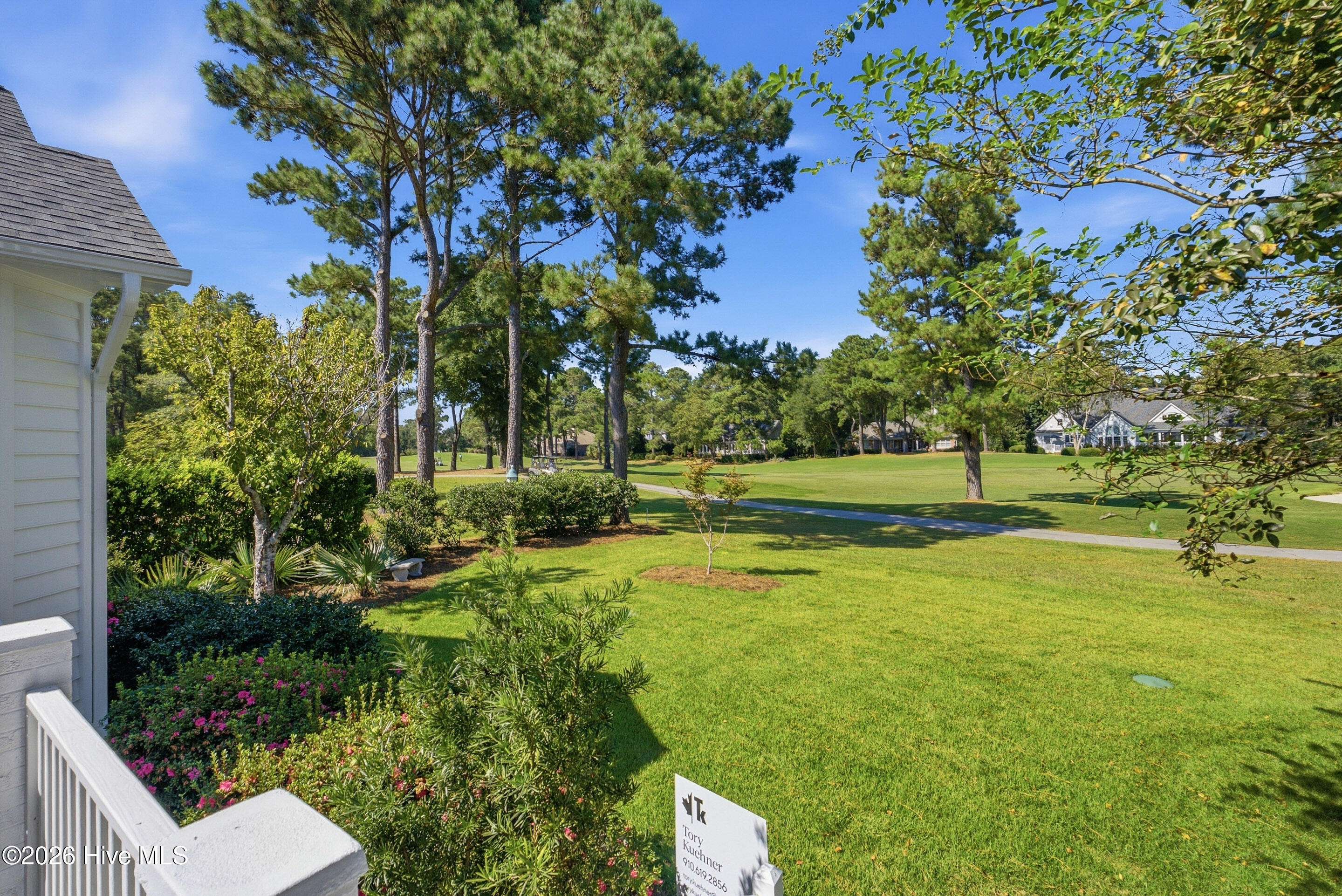 Landscaped lawn beside the home overlooks a golf course, with tall pines and a paved cart path.
