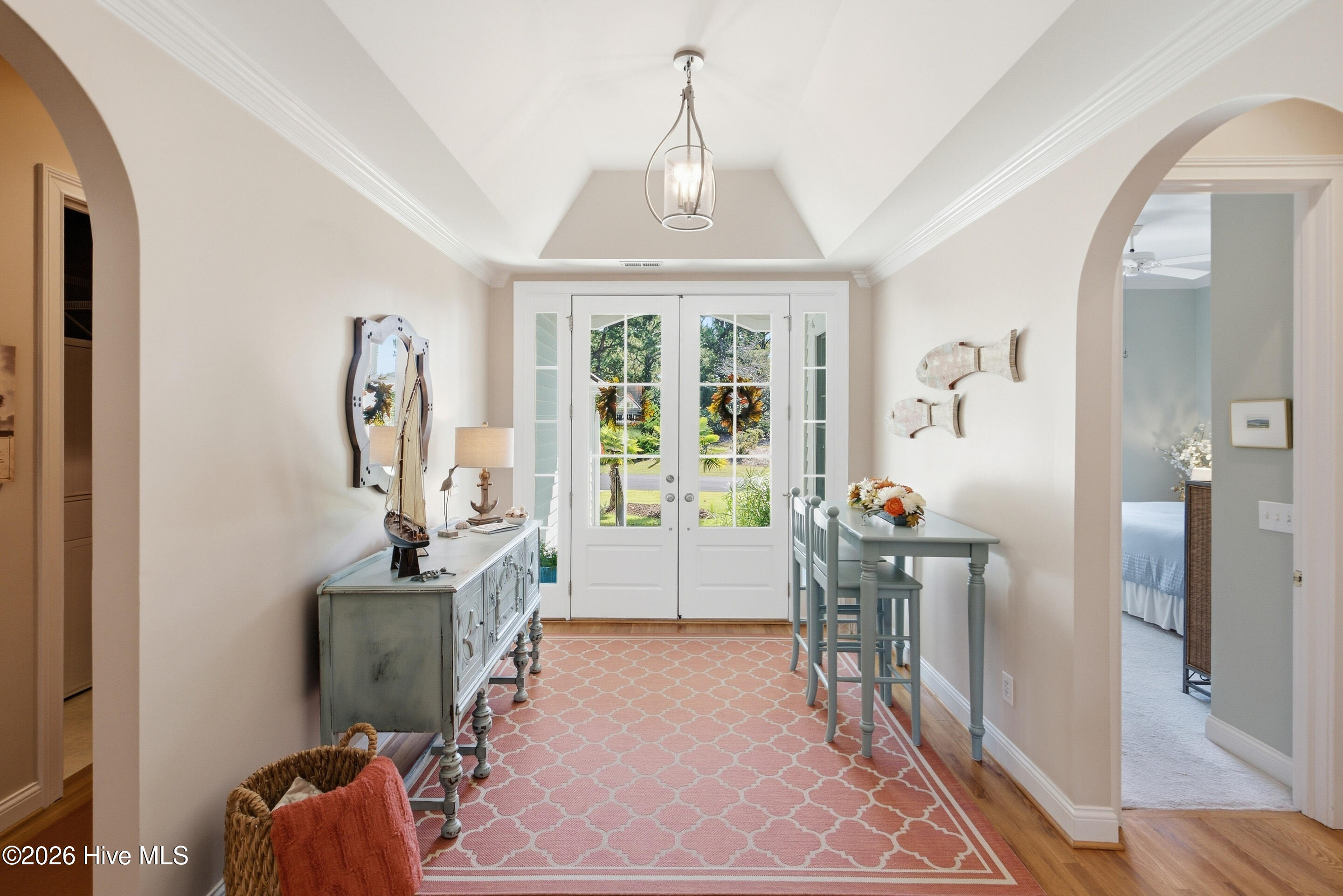 Entry hall with white French doors, a coral patterned rug, and pale blue furnishings.