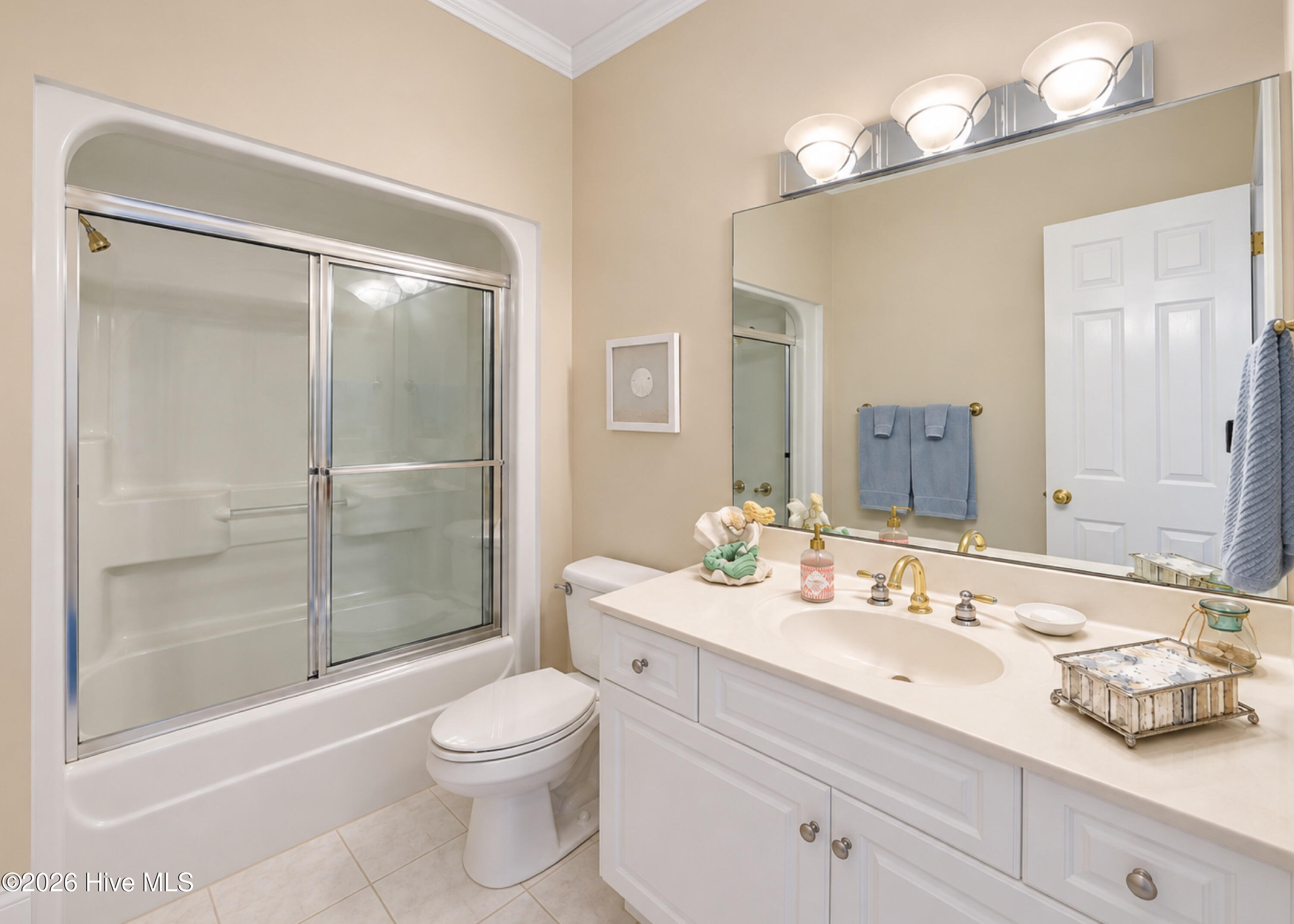 Bathroom with a white vanity, large mirror, toilet, and bathtub with sliding glass shower doors.