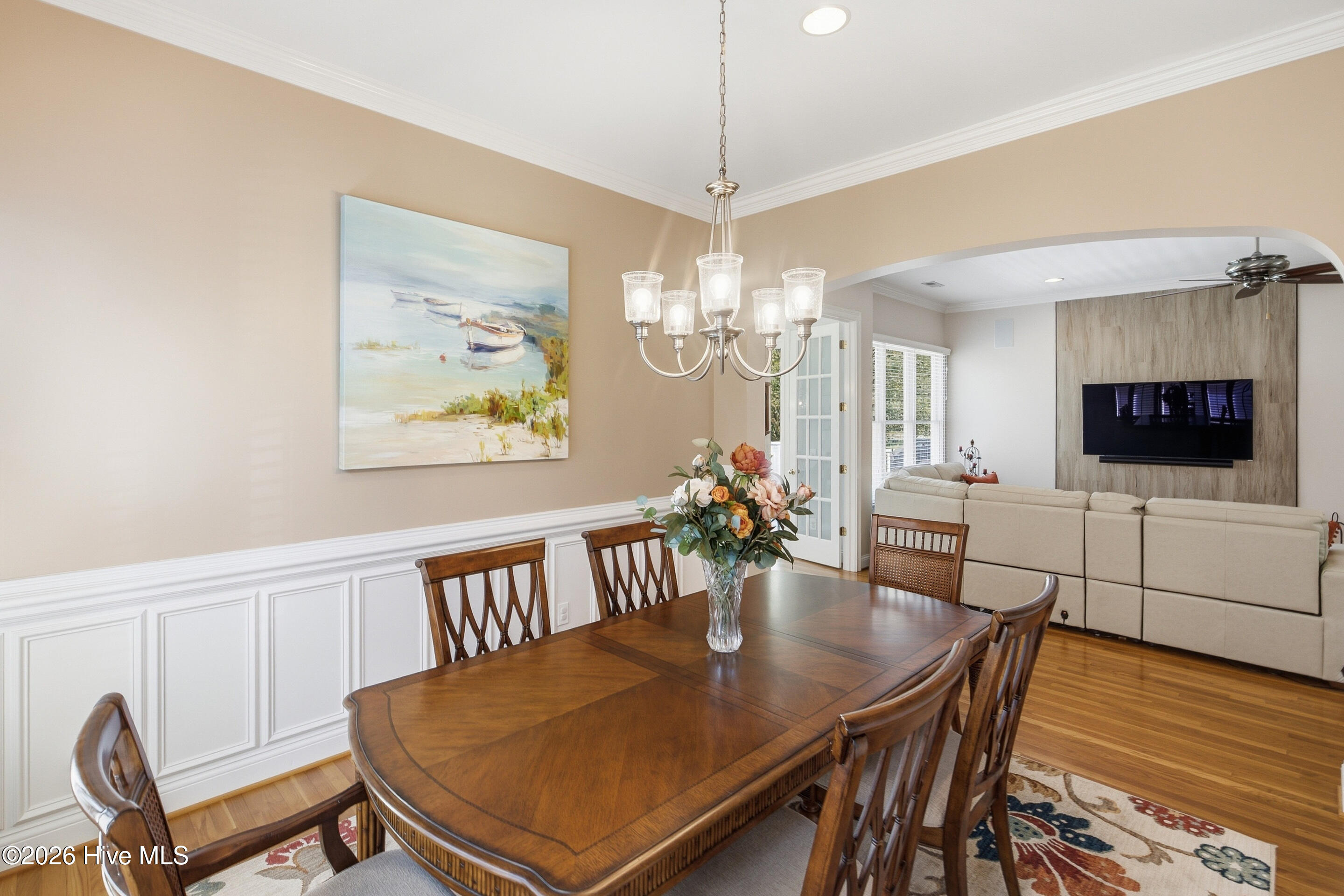 Dining room with a dark wood table and chandelier, opening into a living room with a beige sectional.