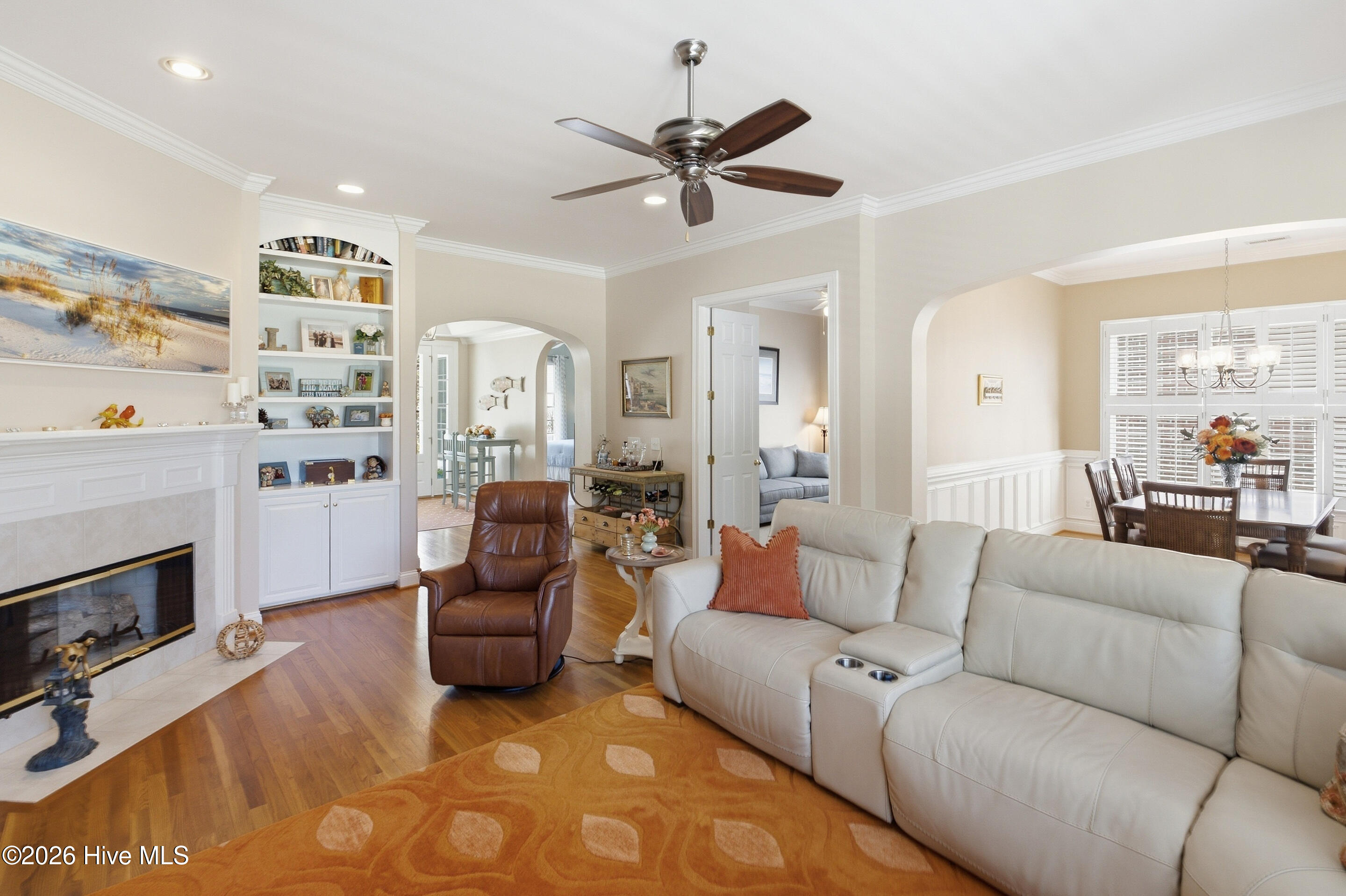 Furnished living room with a white sectional, fireplace, built-in shelves, and adjoining dining area.