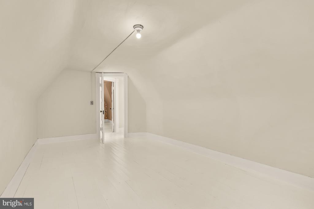 Empty attic room with a sloped ceiling, white flooring and an open doorway.