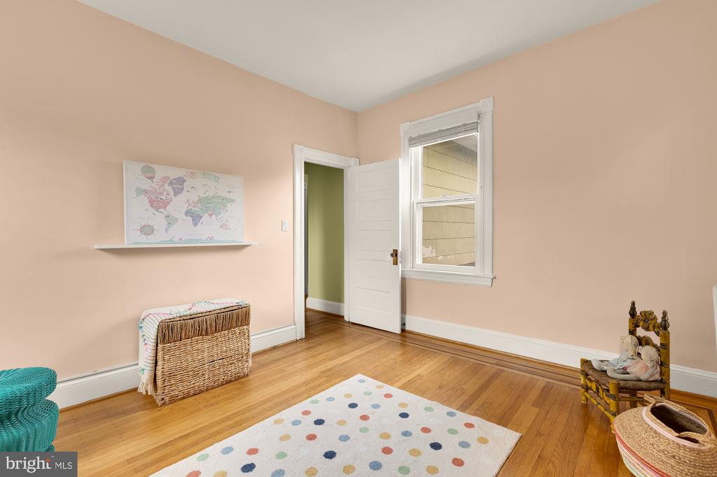 Bedroom with peach walls, hardwood floors, a colorful dotted rug, and a wicker chest.
