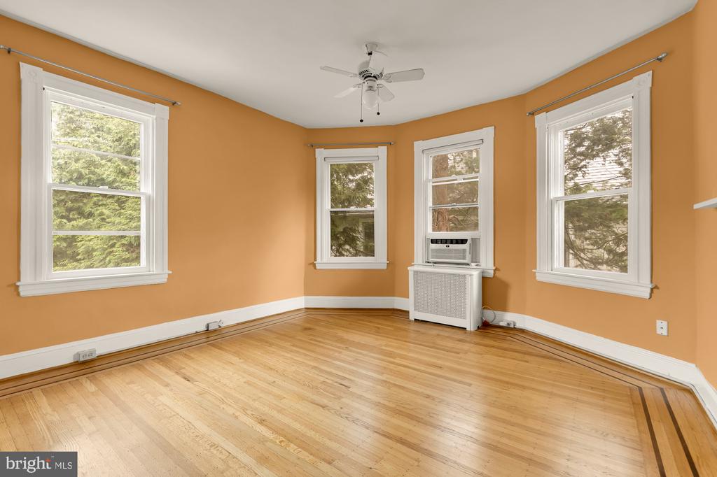 Empty room with orange walls, four windows, a ceiling fan, and bordered hardwood floors.