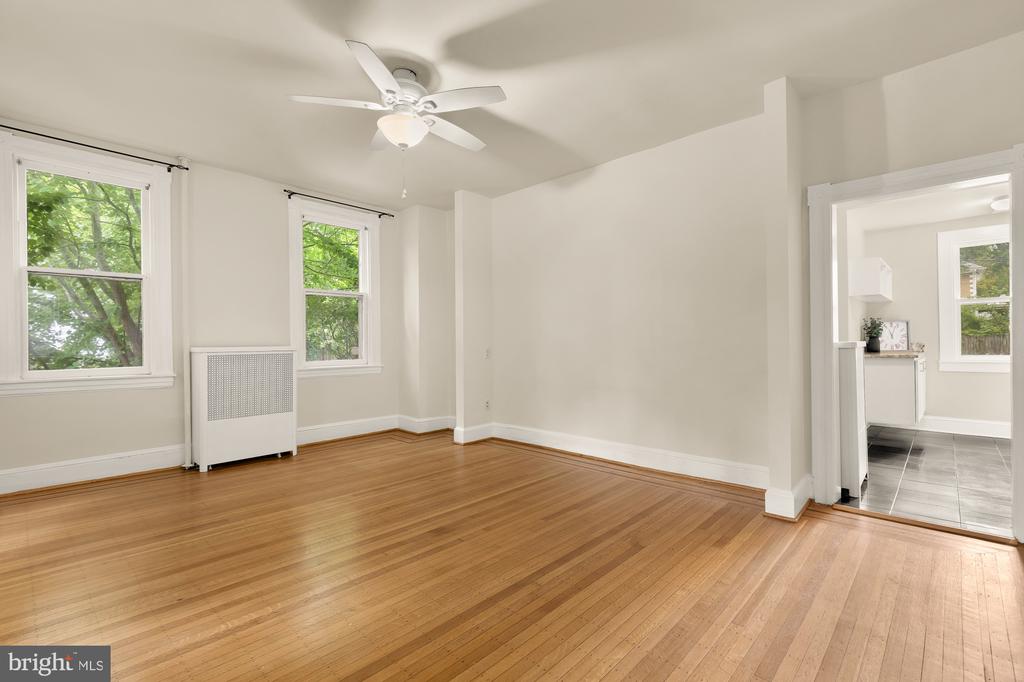 Empty living room with hardwood floors, two windows, and a ceiling fan.